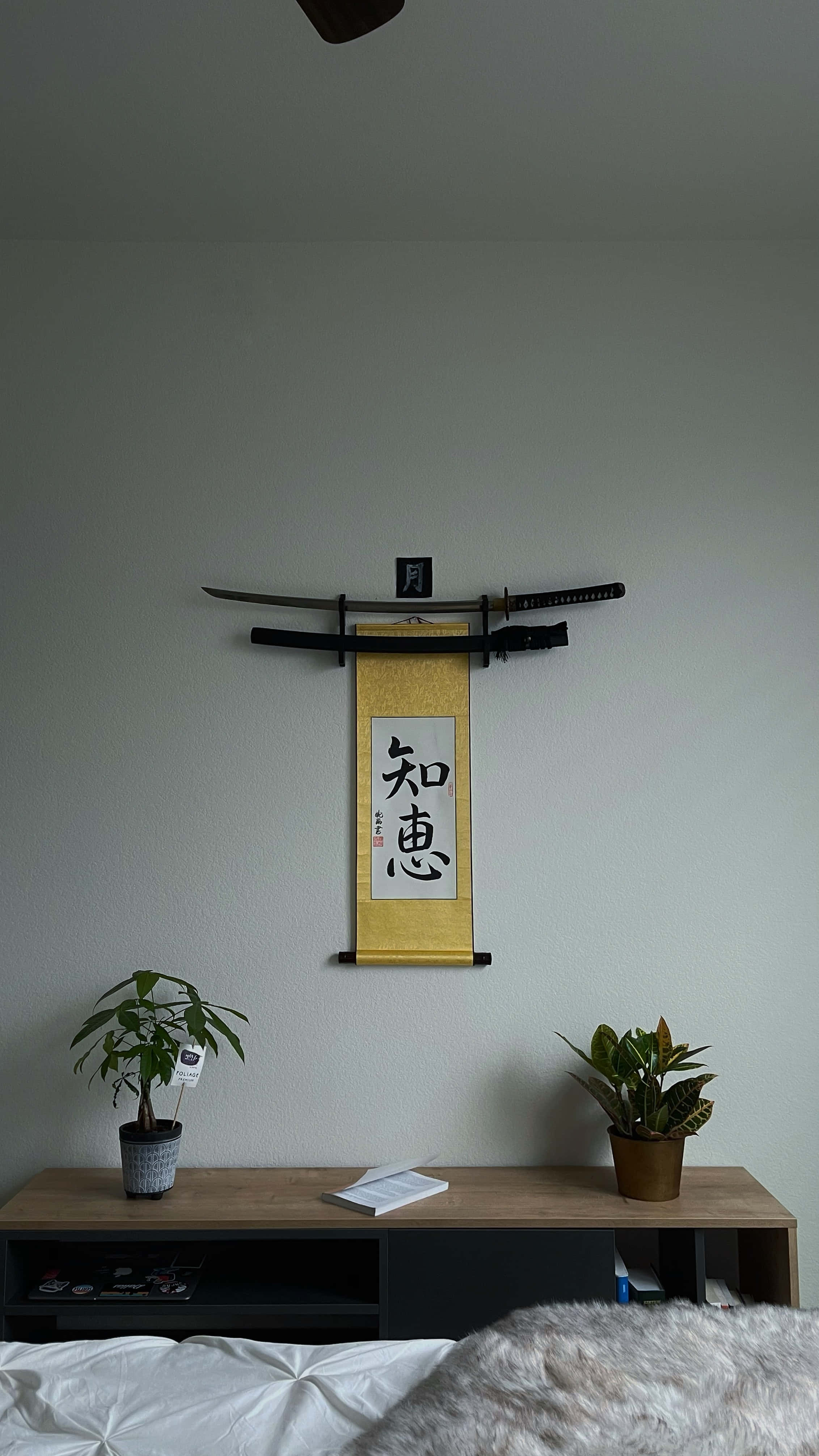 桌布 壁紙 — 簡約風格的臥室牆壁上展示兩把劍，上方懸掛著一幅日本書法卷軸，兩側擺放盆栽植物。