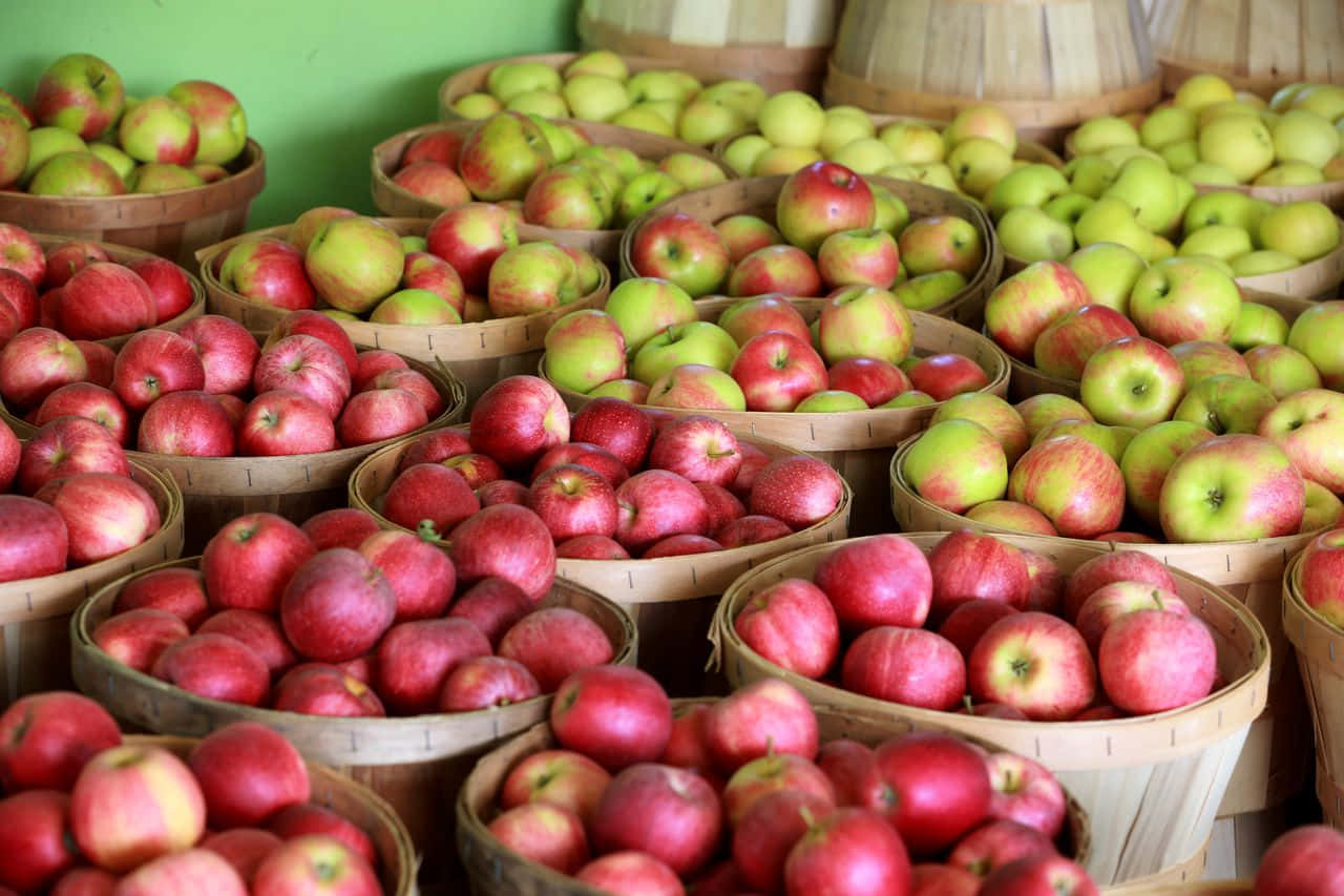 Fall Apples 桌布 壁紙 — 籃子裡裝滿了鮮紅和翠綠的蘋果，擺放在色彩繽紛的市場展示中。