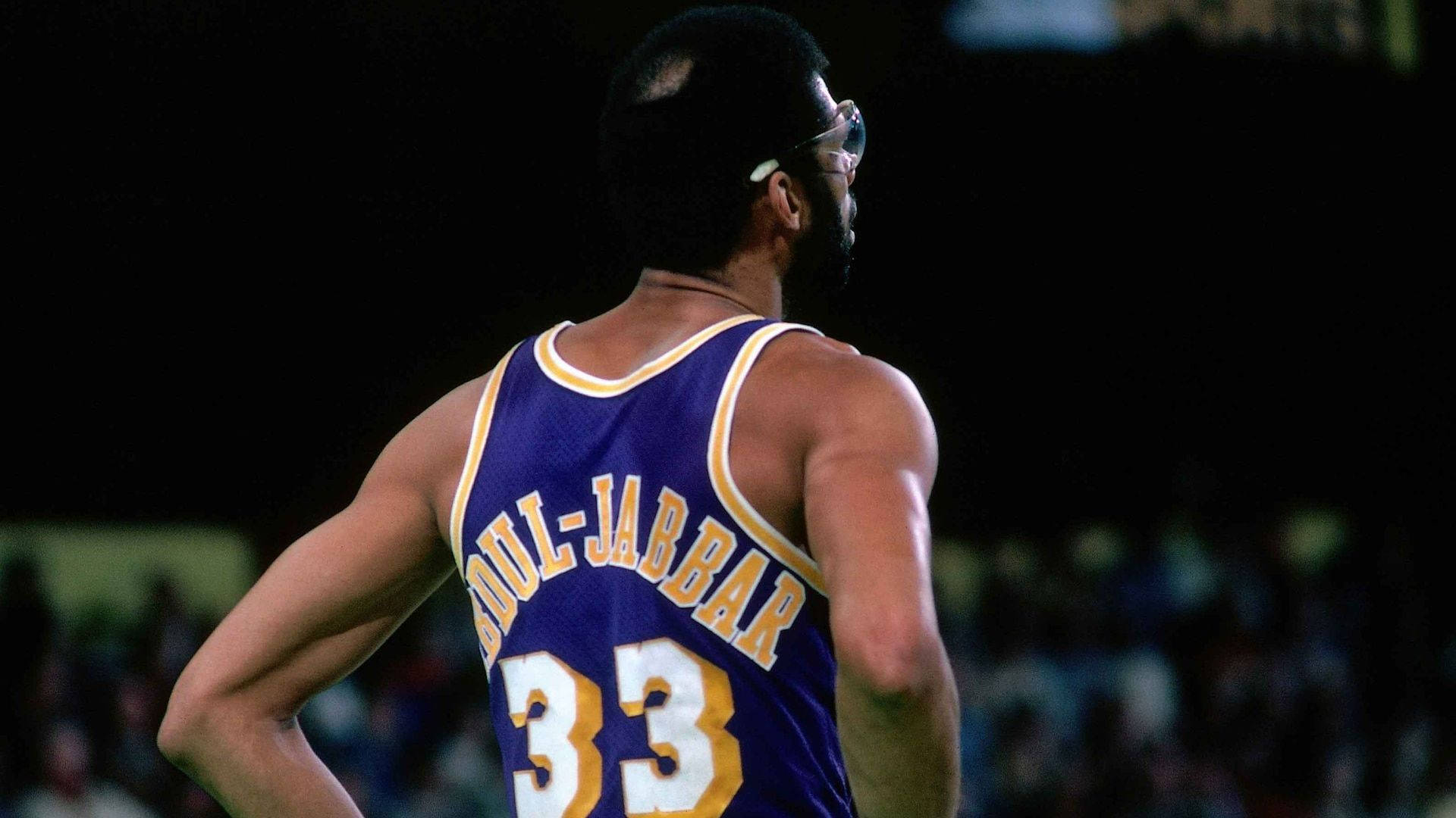 Kareem 桌布 壁紙 — 籃球傳奇威爾特·張伯倫的背面，身穿紫色和金色33號球衣，夜晚站在球場上。