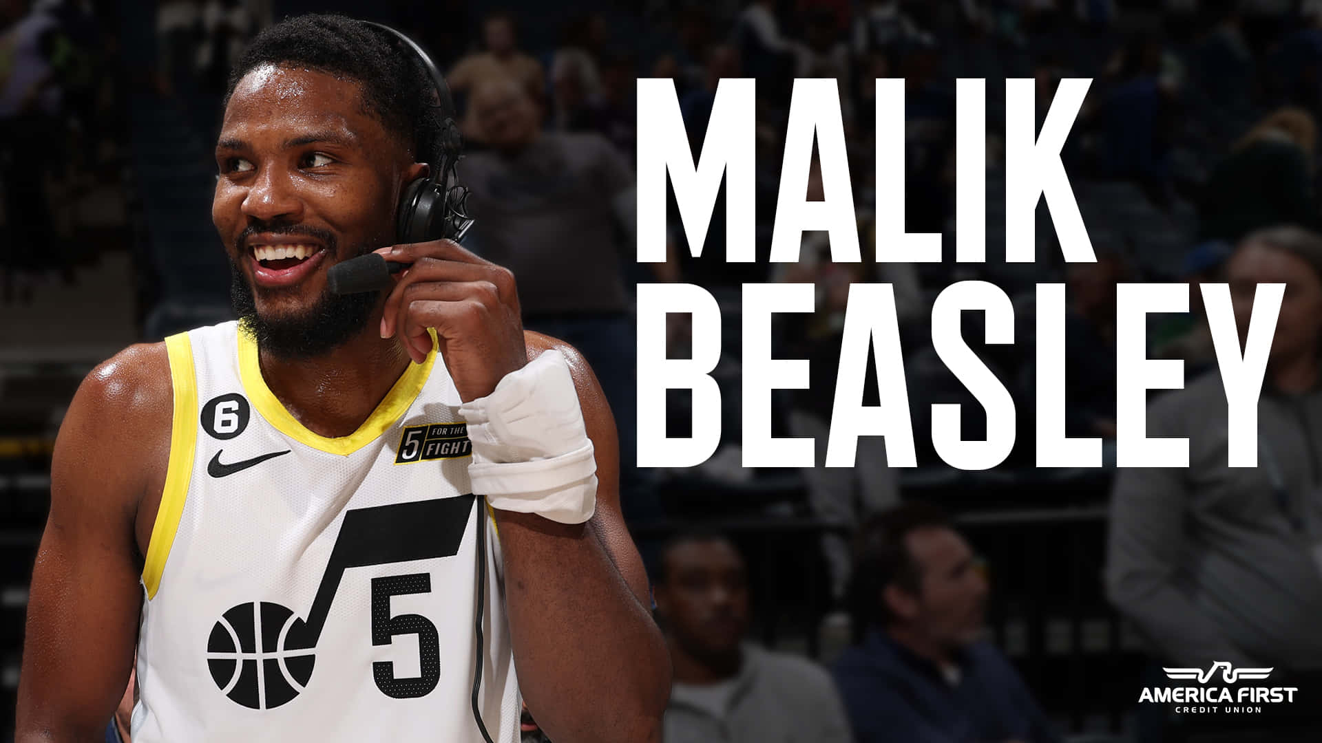 籃球 桌布 壁紙 — 籃球運動員 Malik Beasley 在比賽中戴著耳機，身穿白色和黃色5號球衣，露出燦爛的笑容。