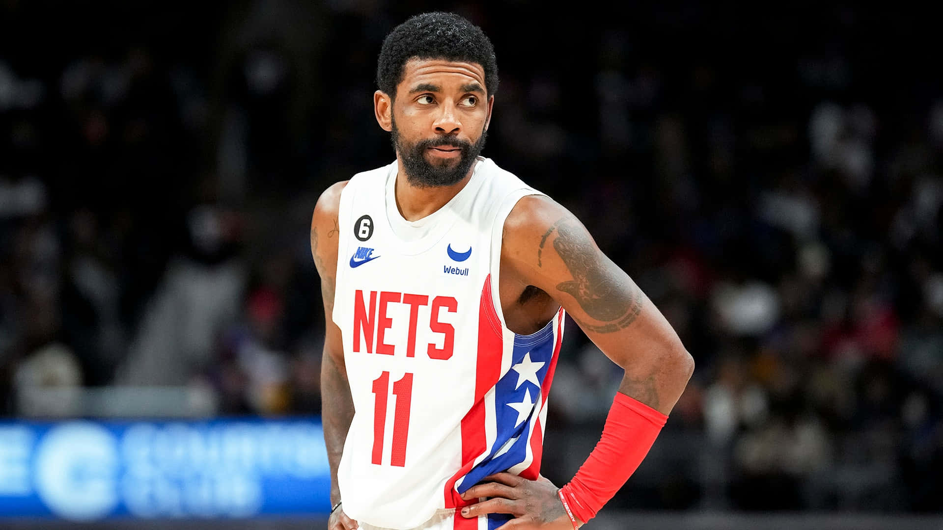 Kyrie Irving Nets 桌布 壁紙 — 籃球運動員凱里·厄文身穿白色、紅色和藍色的籃網隊11號球衣，在比賽中專注地站在球場上。