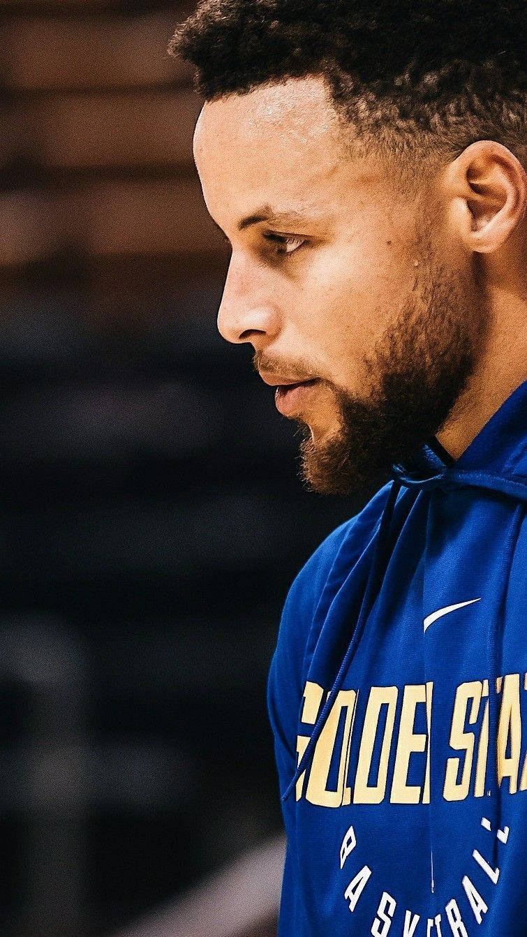 Curry 桌布 壁紙 — 籃球運動員史蒂芬柯瑞的特寫肖像，身穿藍色金州勇士連帽衫，低頭專注的表情。