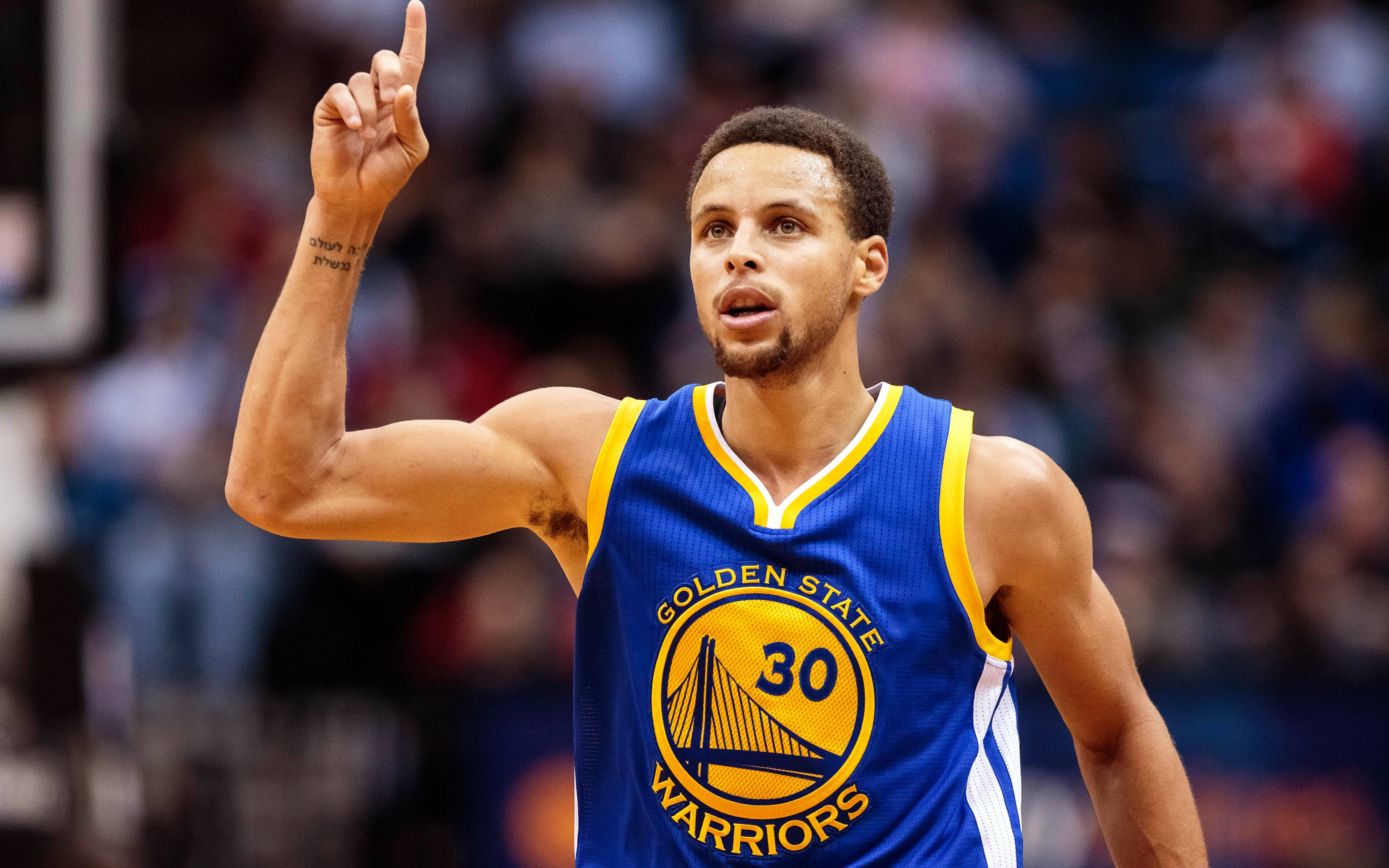 4K NBA 桌布 壁紙 — 籃球運動員史蒂芬柯瑞身穿金州勇士隊球衣，在比賽中向上指，背景有觀眾。