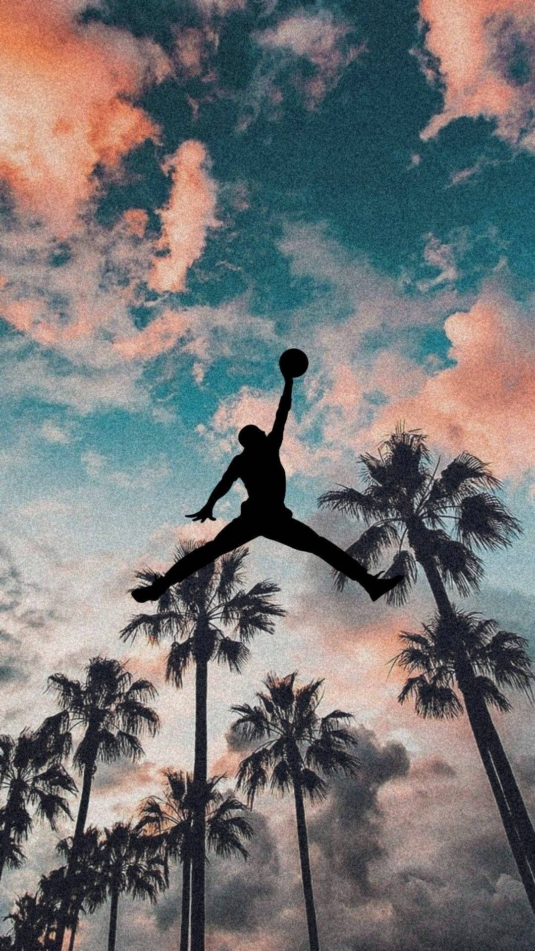 Jordan Logo 桌布 壁紙 — 籃球運動員在半空中灌籃的剪影，背景是充滿活力的日落天空和棕櫚樹。