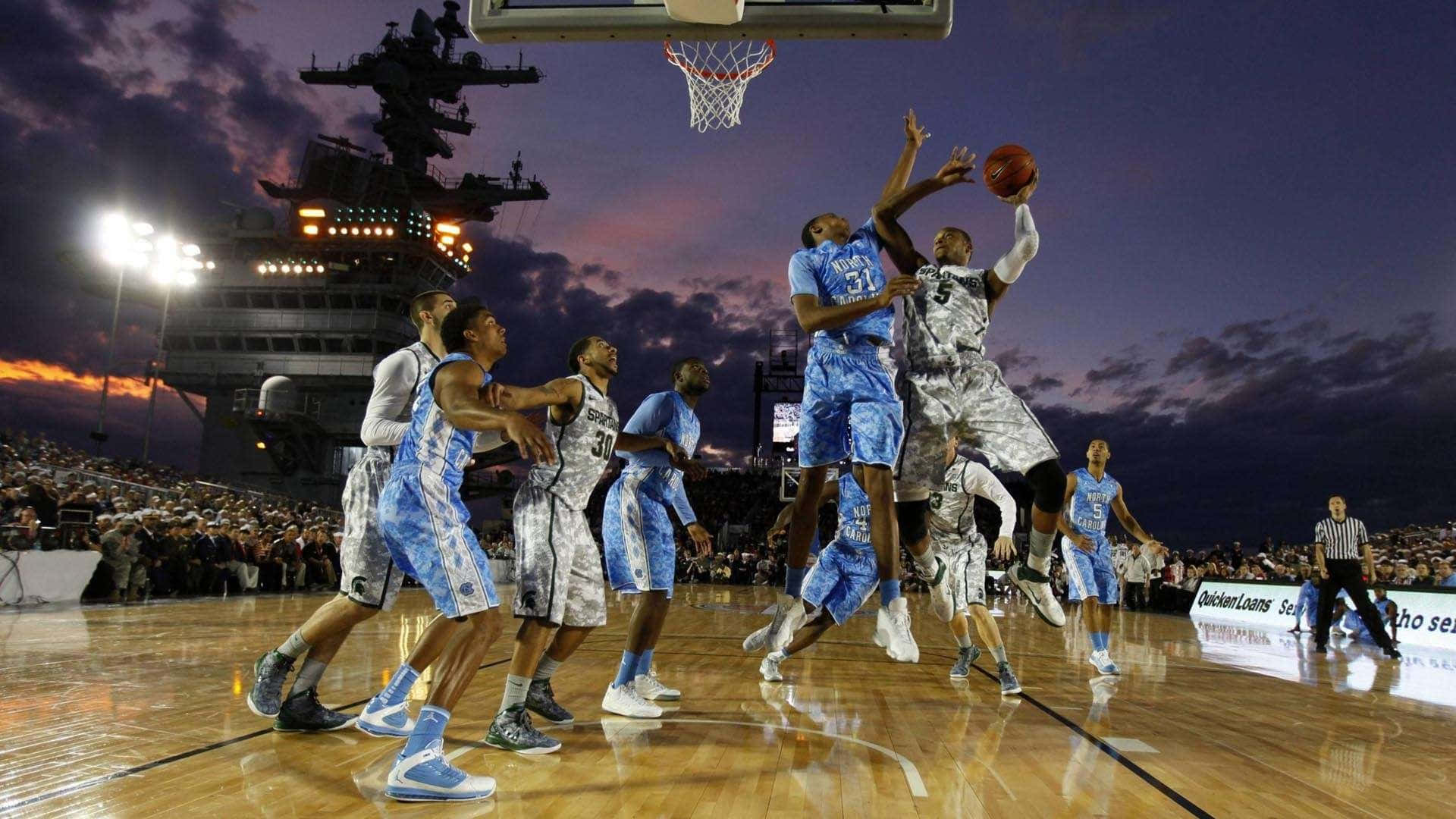 1080p Basketball 桌布 壁紙 — 籃球運動員在體育館燈光下跳起投籃，暮色天空中隱約可見一艘航空母艦。