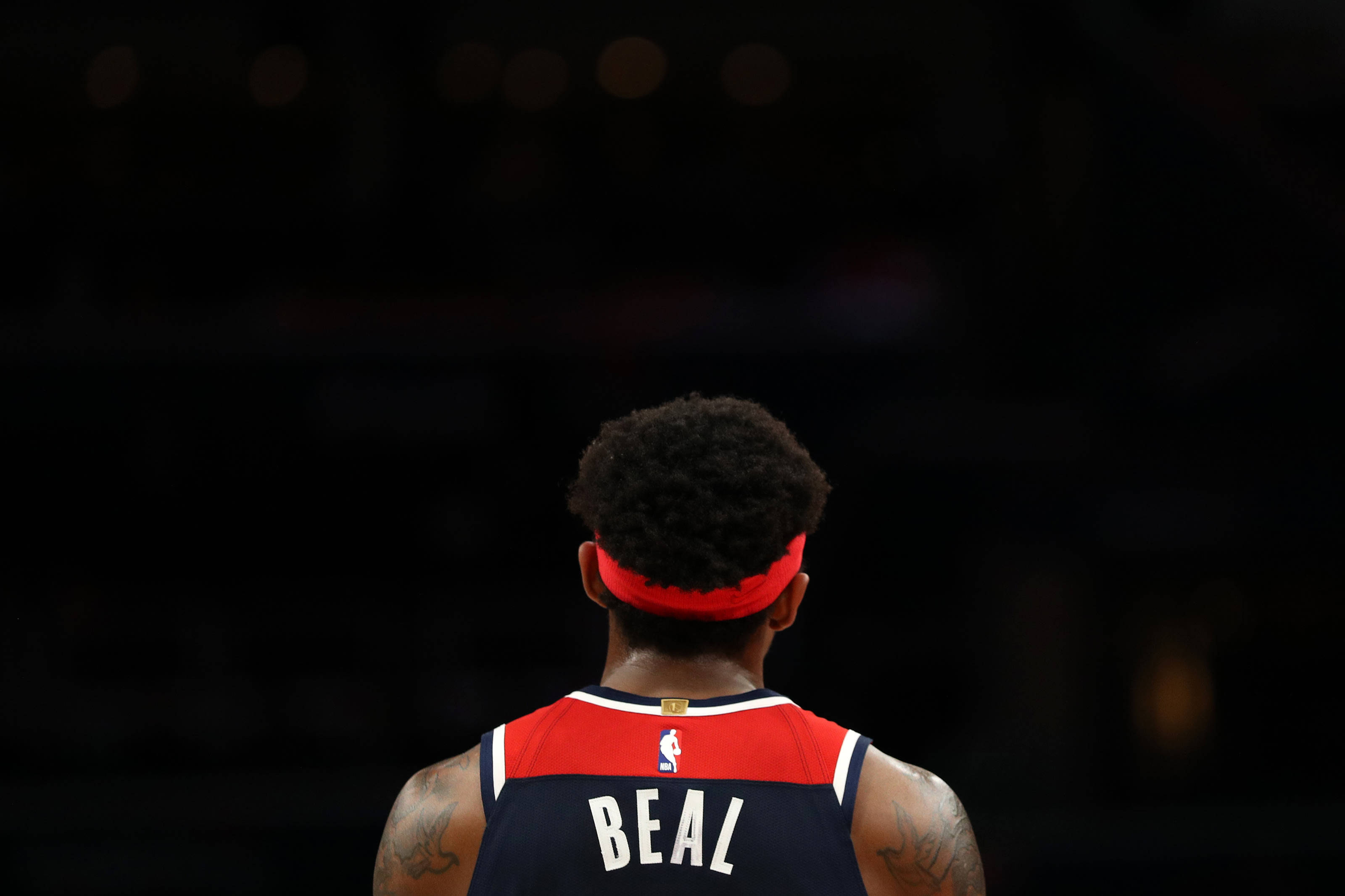 Bradley Beal 桌布 壁紙 — 籃球運動員比爾身穿紅色和海軍藍球衣，獨自站在昏暗的場館聚光燈下的背影。
