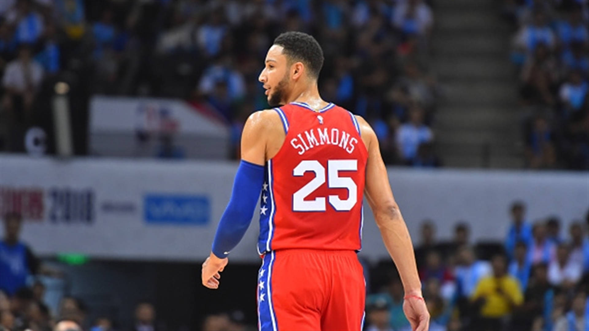 NBA 桌布 壁紙 — 籃球運動員班·西蒙斯身穿紅藍色25號球衣，在球場上背對鏡頭走開，身後是模糊的人群。