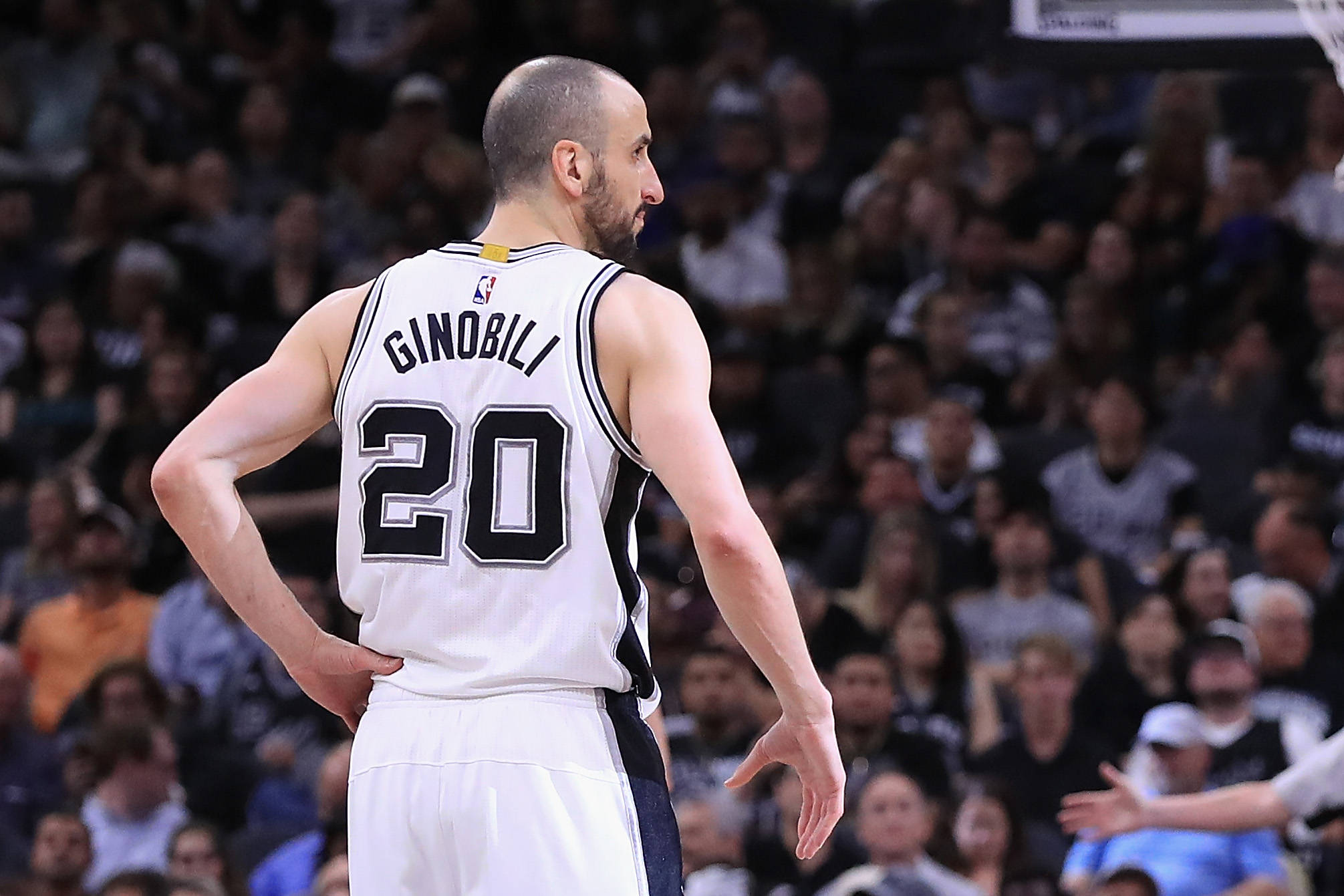 Manu 桌布 壁紙 — 籃球運動員馬努·吉諾比利身穿白色馬刺隊20號球衣，雙手叉腰面向場館內的人群站立。