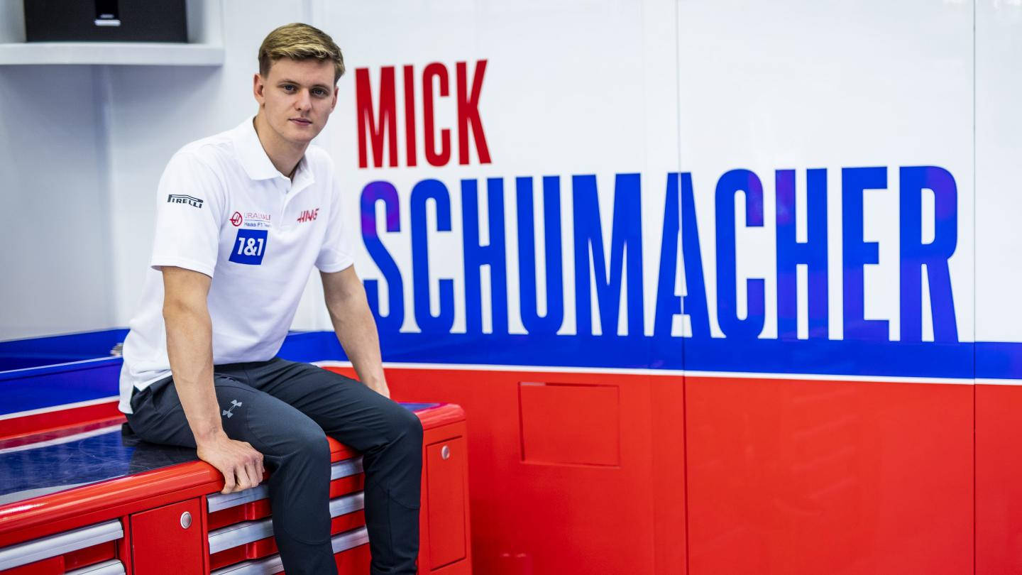 mick schumacher 桌布 壁紙 — 米克舒馬赫自信地坐在車庫的紅色工具箱上，身後有他名字的粗體紅色和藍色字母。