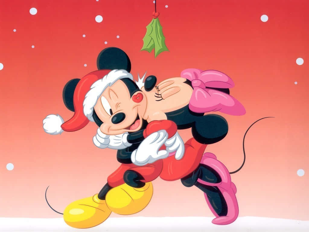 Mickey And Minnie Mouse 桌布 壁紙 — 米奇和米妮老鼠穿著節日服裝，在飄雪下分享一個快樂的親吻，上方有冬青裝飾。
