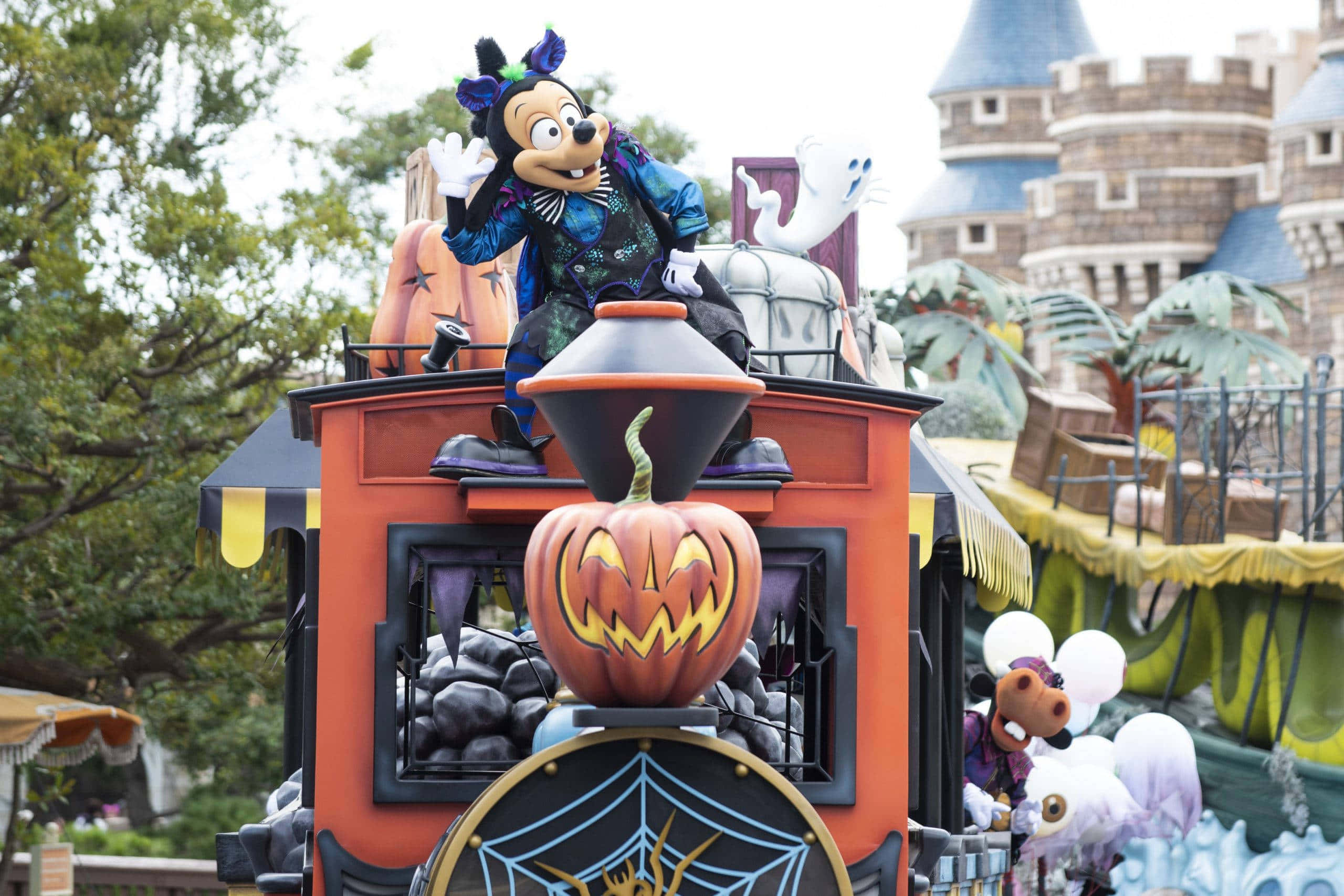 Halloween Parades 桌布 壁紙 — 米奇老鼠穿著萬聖節服裝，在裝飾著南瓜、鬼魂和蜘蛛網的節日橙色遊行花車上揮手。
