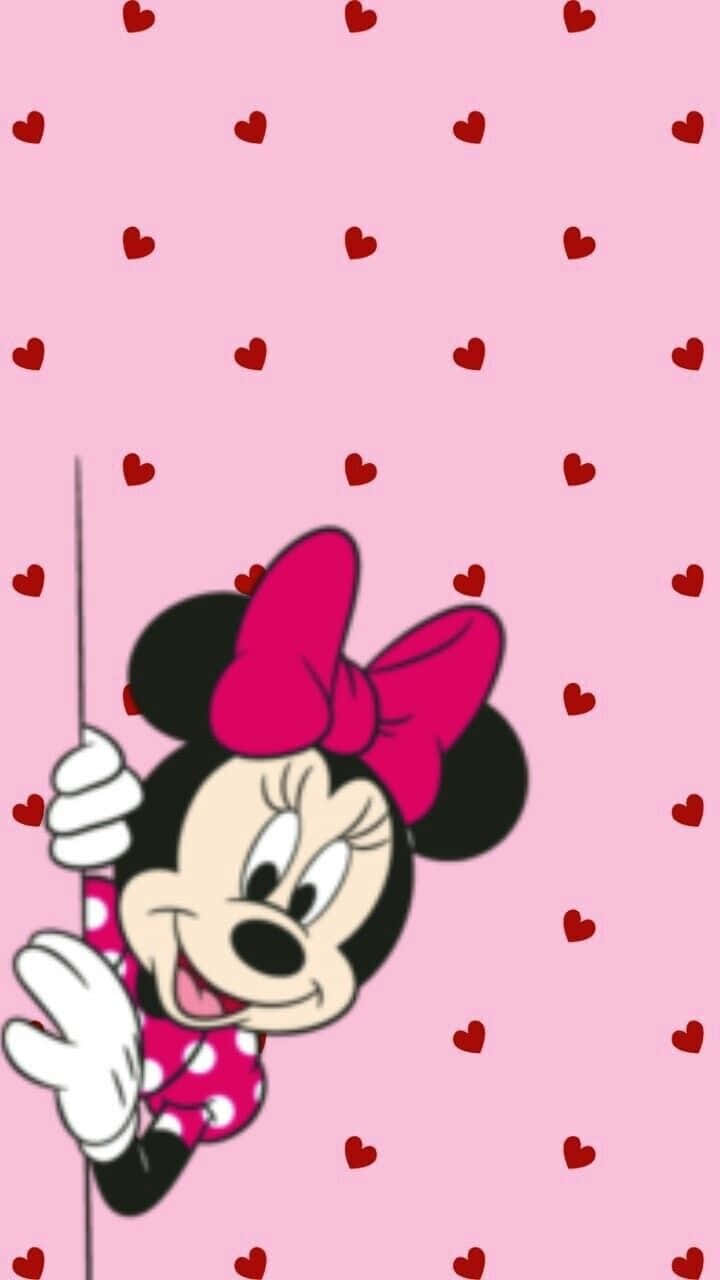 Minnie Mouse Pink 桌布 壁紙 — 米妮老鼠在一個有紅色愛心點綴的粉紅色背景後面，開心地從一根柱子後面探出頭來。