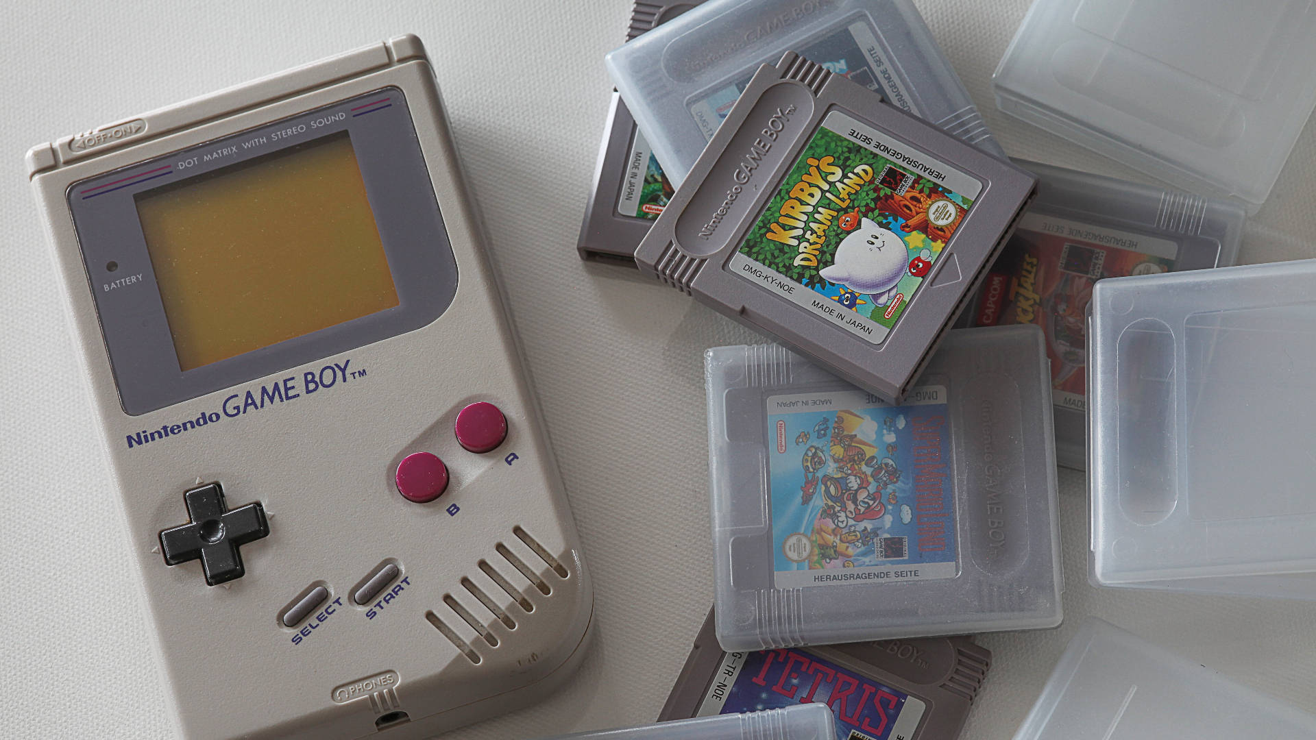 game 桌布 壁紙 — 米色 Game Boy 連同卡帶，包括 Kirby's Dream Land 和 Tetris，散落在白色表面上。