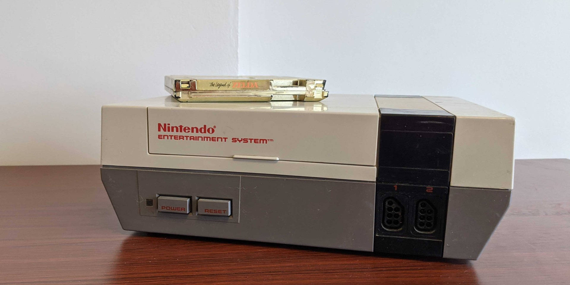 紅白機 桌布 壁紙 — 米色 Nintendo Entertainment System 主機放在木桌上，上面放著一個金色遊戲卡帶。