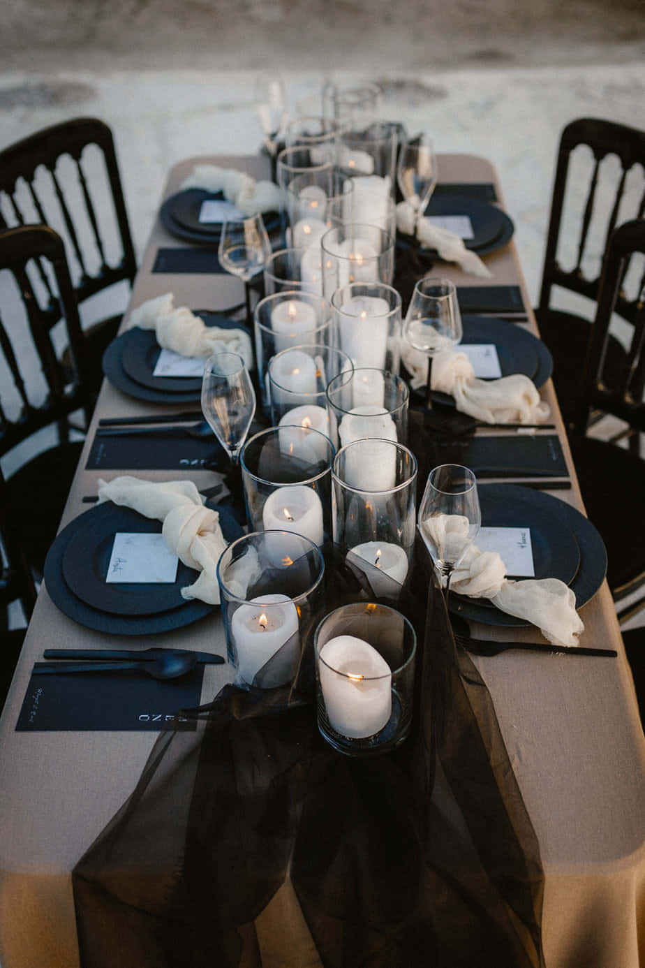 Black And White Wedding 桌布 壁紙 — 米色桌布上帶有玻璃燭台內點燃蠟燭的優雅黑白餐桌佈置。
