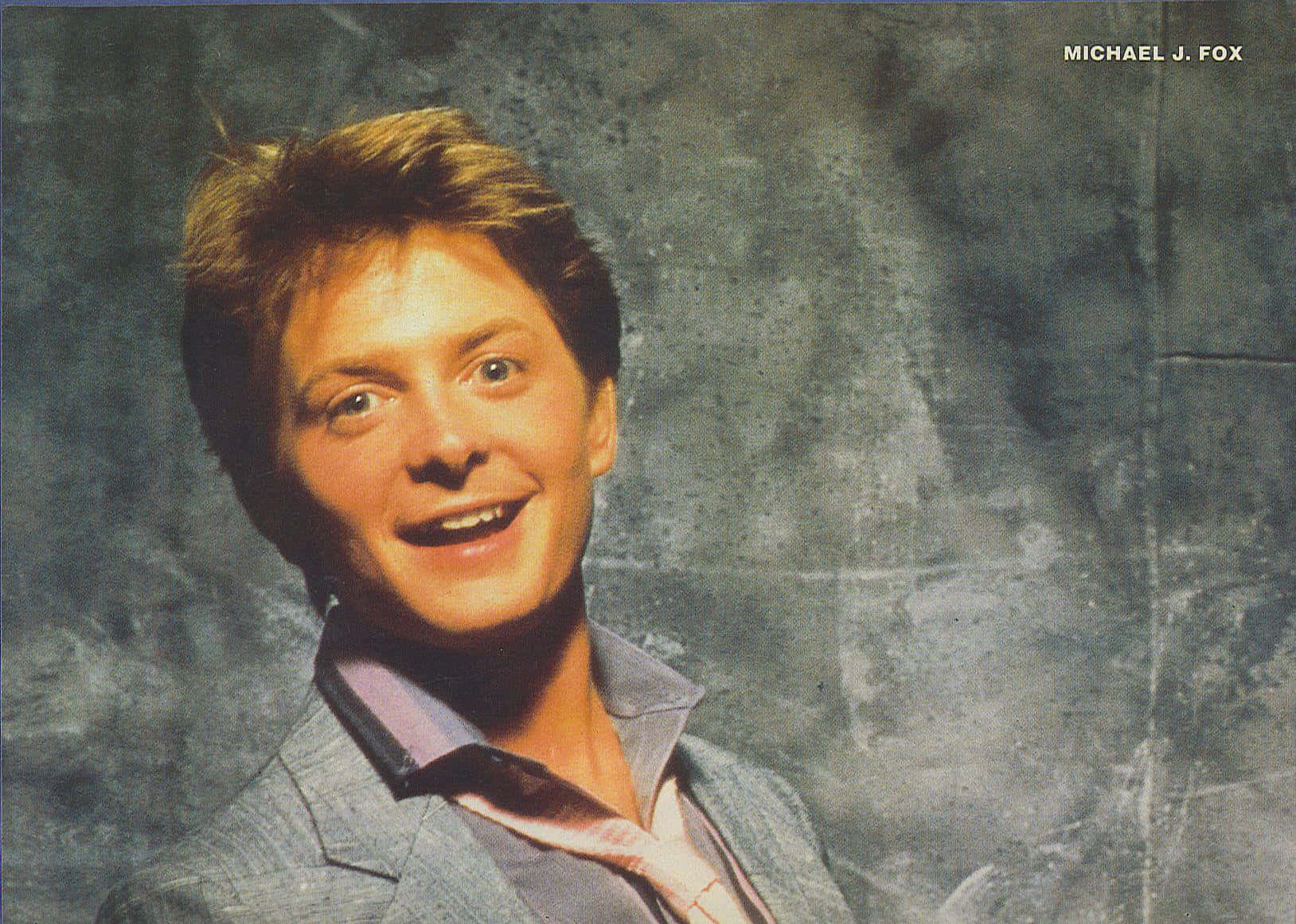 michael j fox 桌布 壁紙 — 米高·J·福克斯在紋理灰色背景上露出燦爛笑容，身穿淺灰色西裝和開領襯衫。