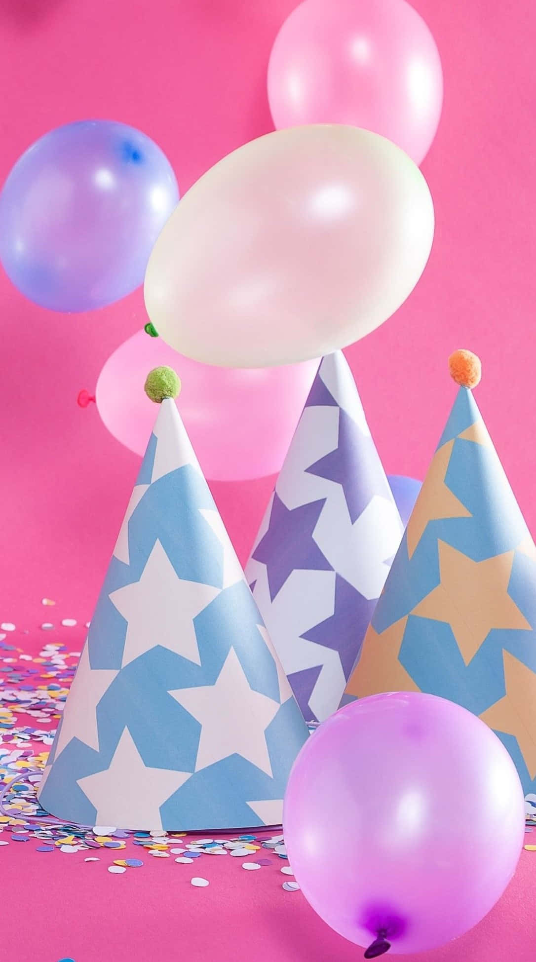 Pink Birthday 桌布 壁紙 — 粉彩氣球和星星圖案的派對帽在充滿活力的粉紅色背景上，伴隨著五彩紙屑漂浮。