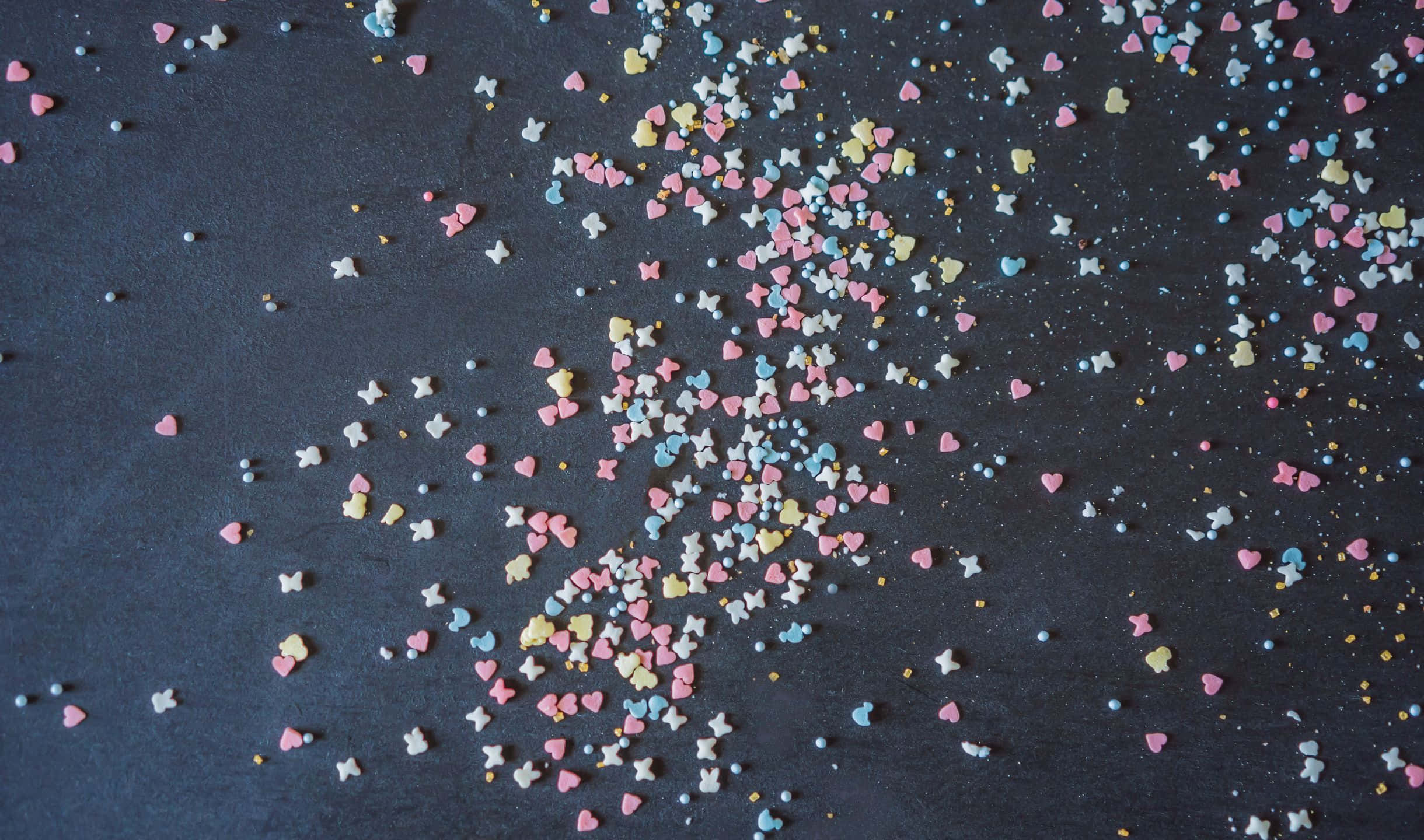 Sprinkles 桌布 壁紙 — 粉彩色心形和星星糖粒散落在深色石板表面上，呈現節日般的爆發感。