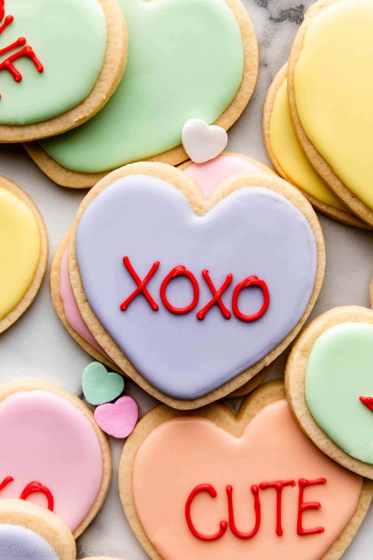 愛心 桌布 壁紙 — 粉彩色心形餅乾，上面有紅色糖霜訊息如 XOXO 和 CUTE，排列在大理石表面上。