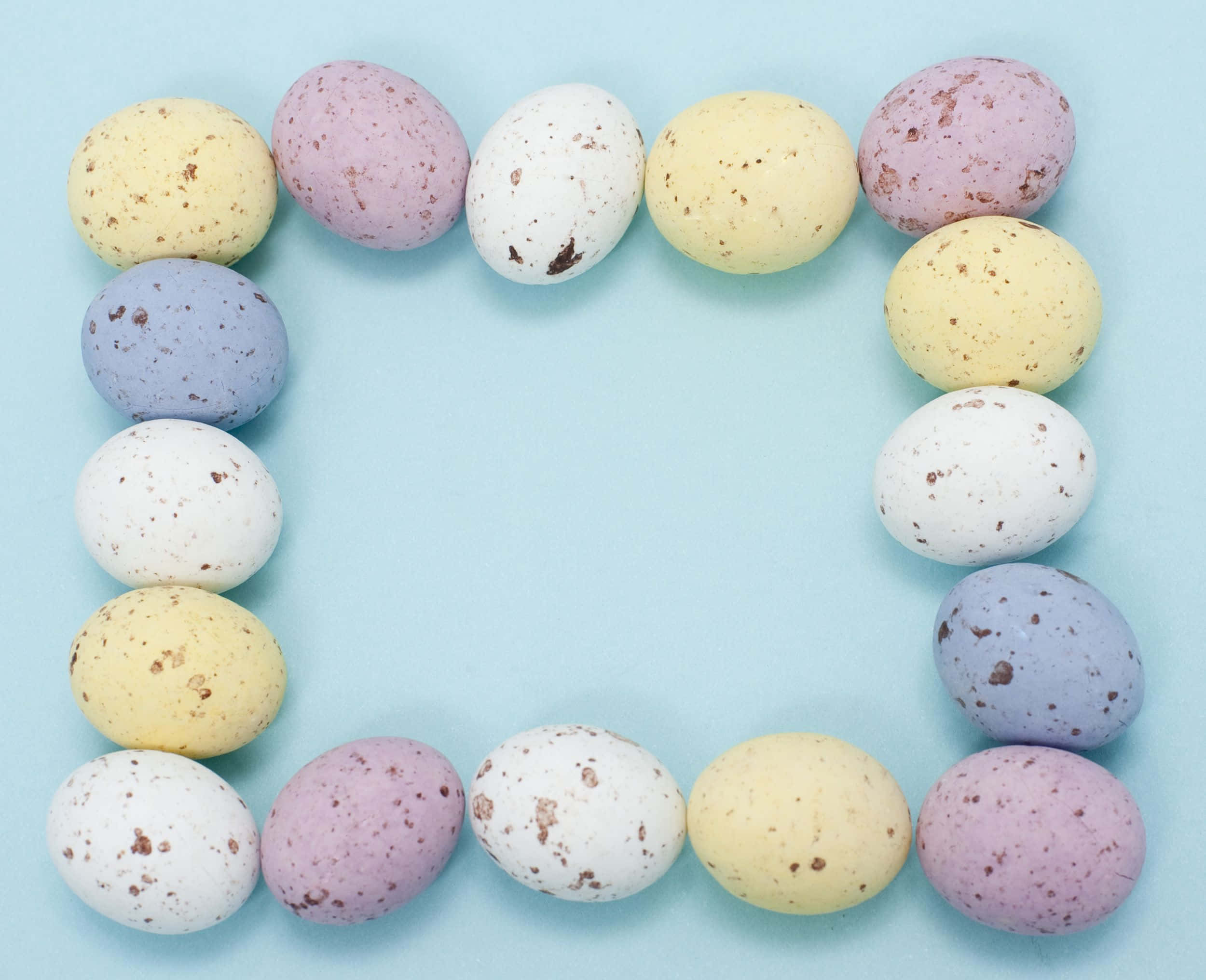 Pastel Easter 桌布 壁紙 — 粉彩色斑點巧克力蛋在柔和藍色背景上排列成方形框架。