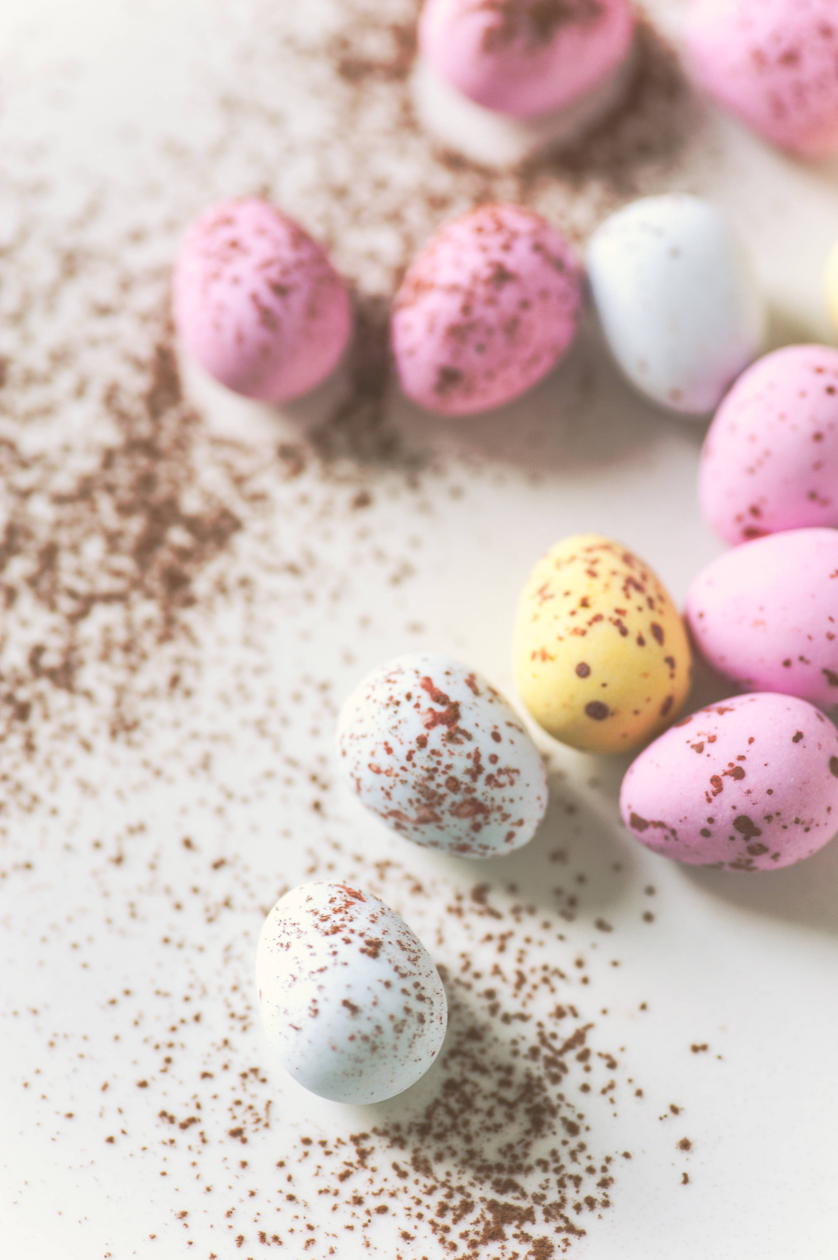 Happy Easter 桌布 壁紙 — 粉彩色斑點巧克力蛋散落在灑有可可粉的白色表面上。