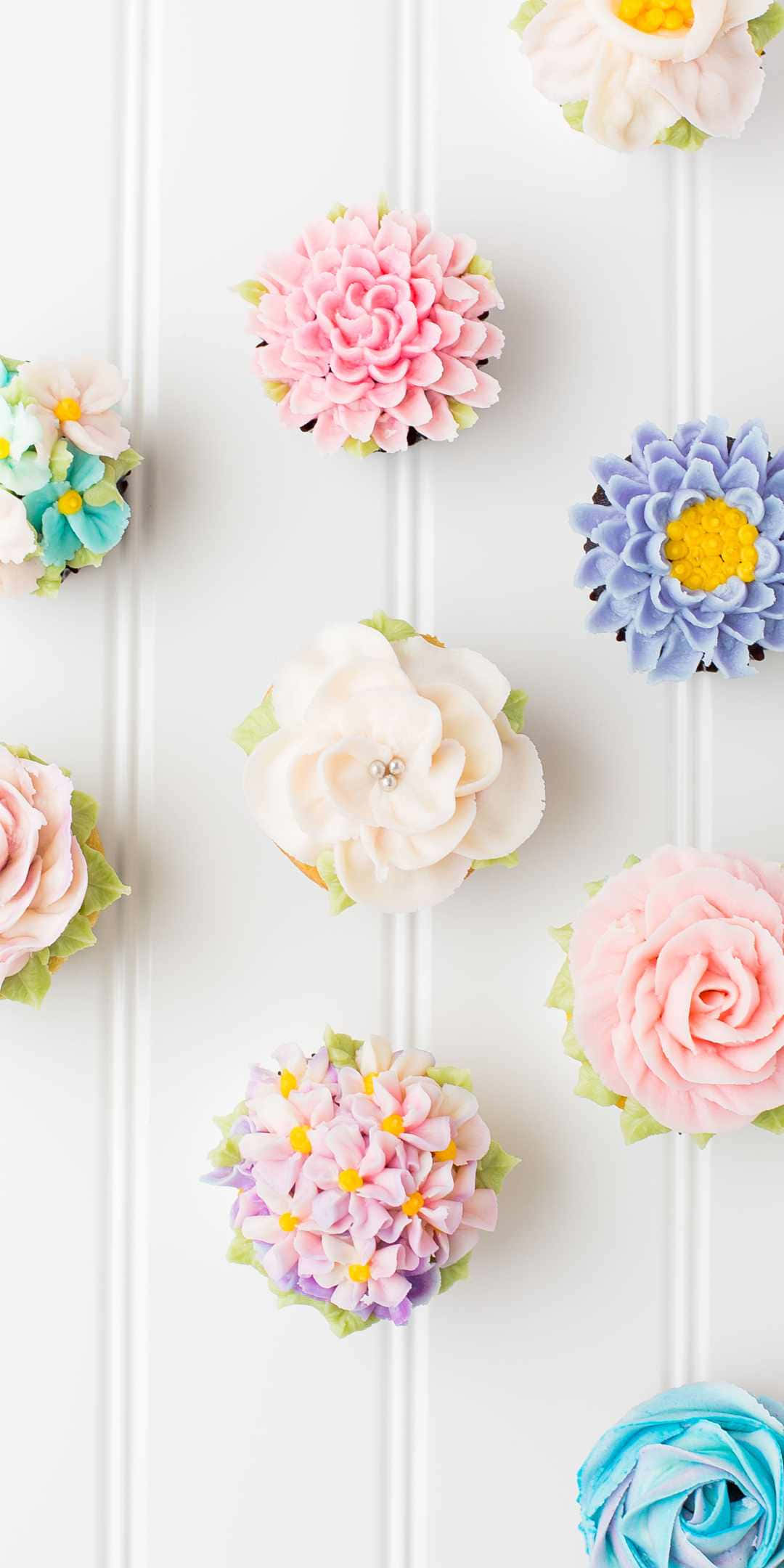 Cupcake 桌布 壁紙 — 粉彩色紙杯蛋糕，上面有精緻的糖花，排列在白色鑲板表面上。