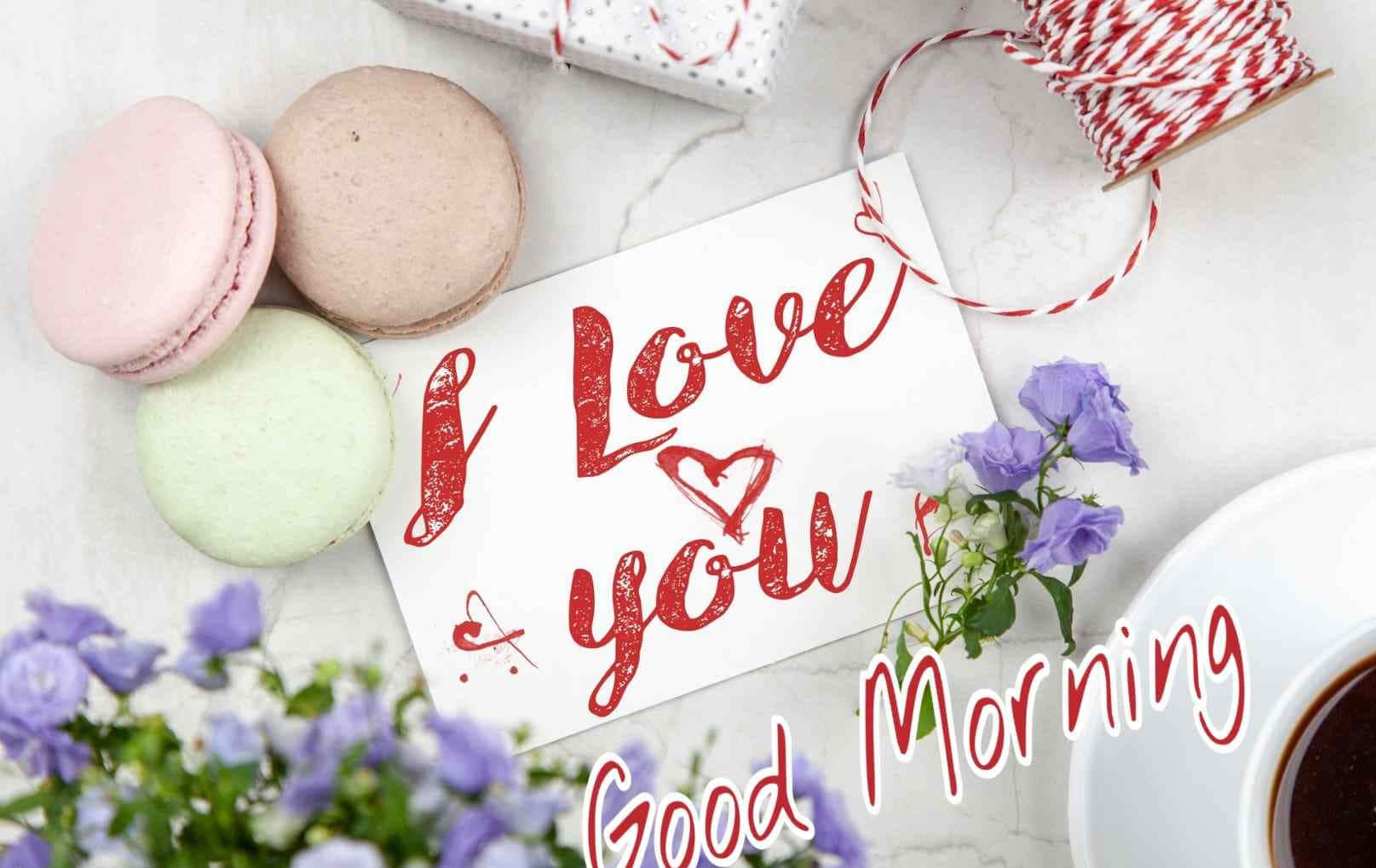 Good Morning 桌布 壁紙 — 粉彩馬卡龍和紫色花朵圍繞著一張手寫的「I Love You Good Morning」卡片，放在大理石表面上。