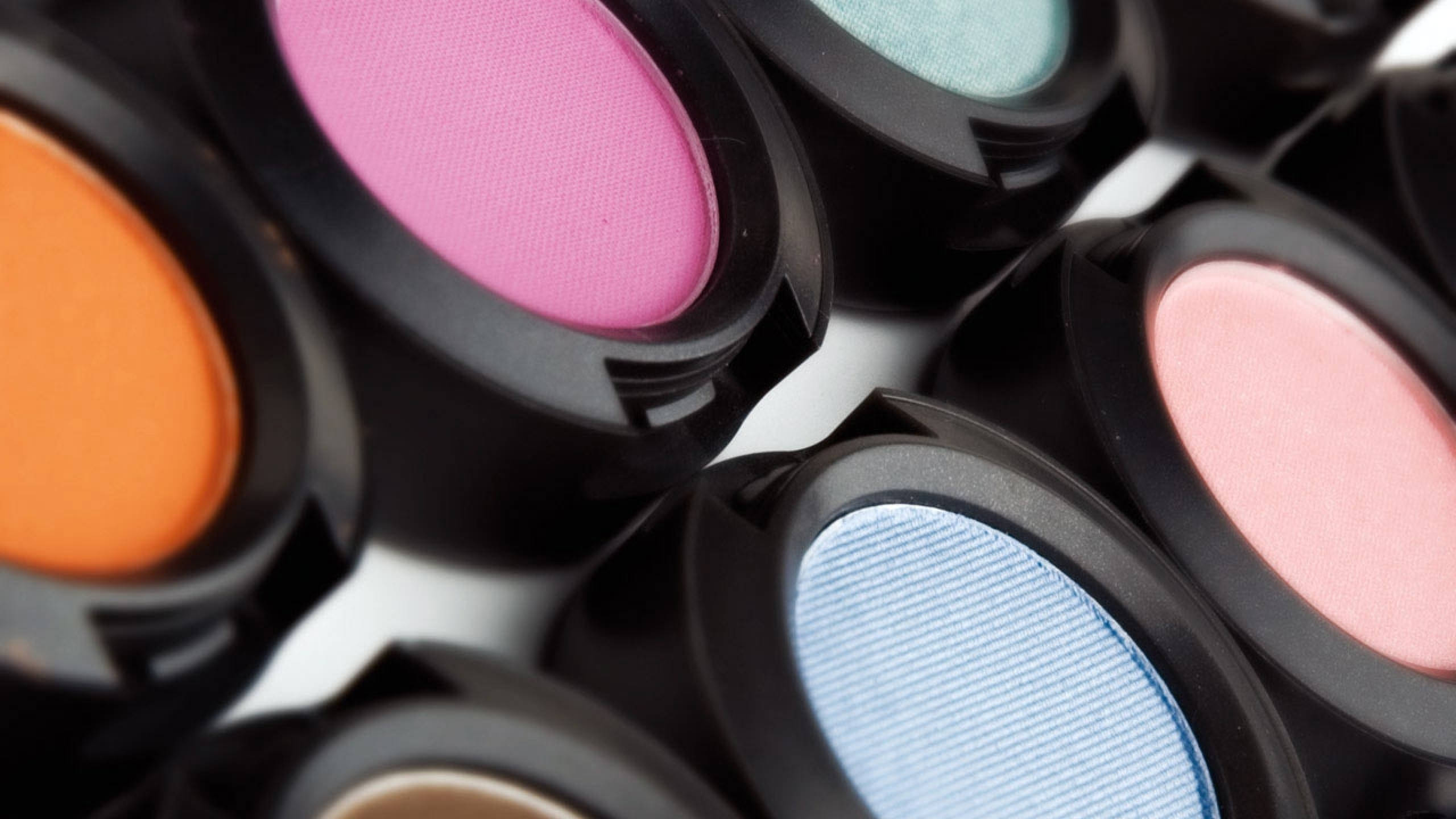 Cosmetics 桌布 壁紙 — 粉紅、橙色、藍色和藍綠色鮮豔眼影盤的特寫，帶黑色蓋子，放在白色表面上。