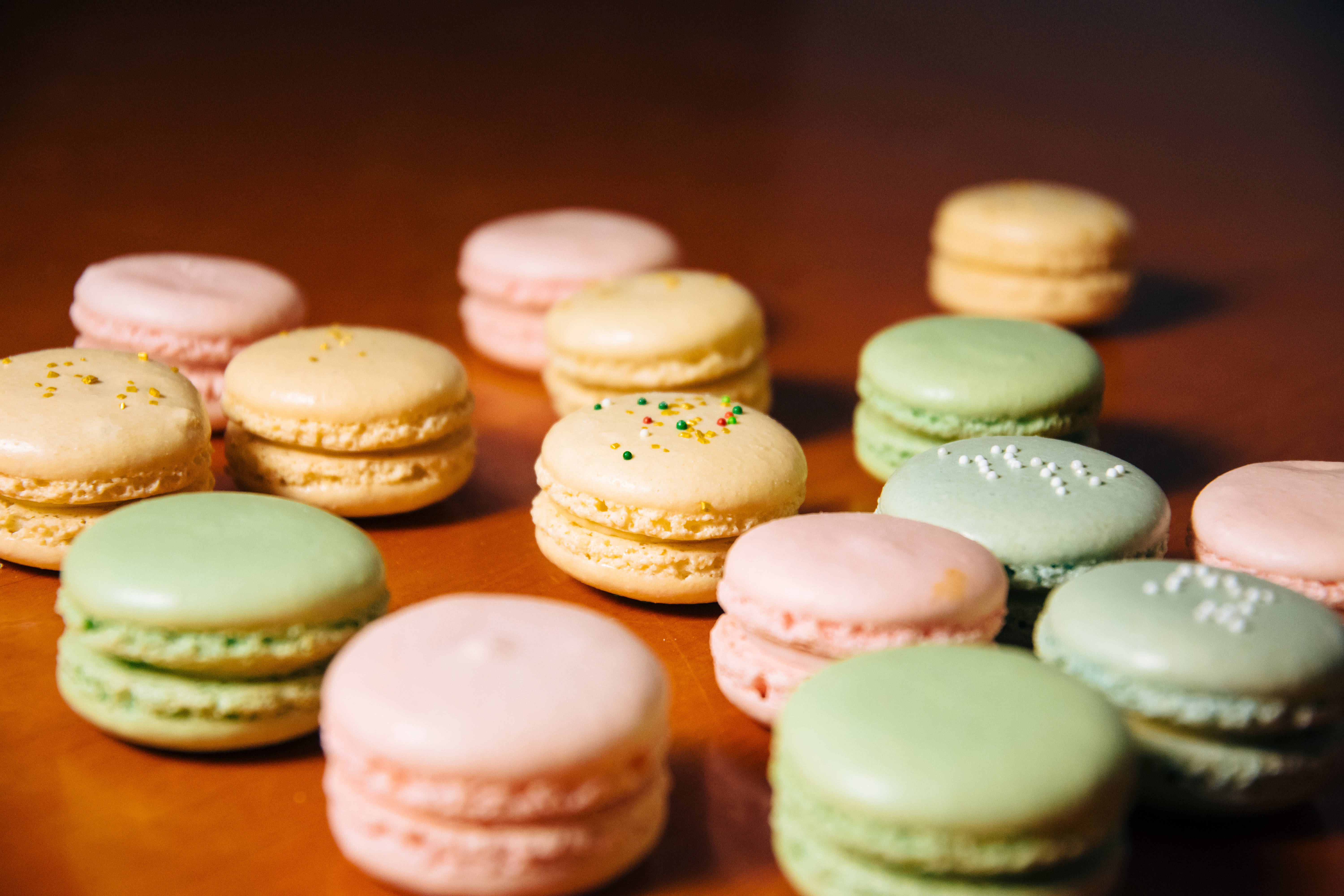 糕點 桌布 壁紙 — 粉紅、綠色和黃色的柔和粉彩馬卡龍，放在溫暖的木質表面上，綴以精緻的糖粒。