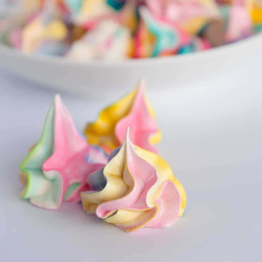 Meringue 桌布 壁紙 — 粉紅、黃色和藍綠色的柔和馬卡龍餅乾在白色表面上呈現鮮豔漩渦，背景有一個模糊的碗。
