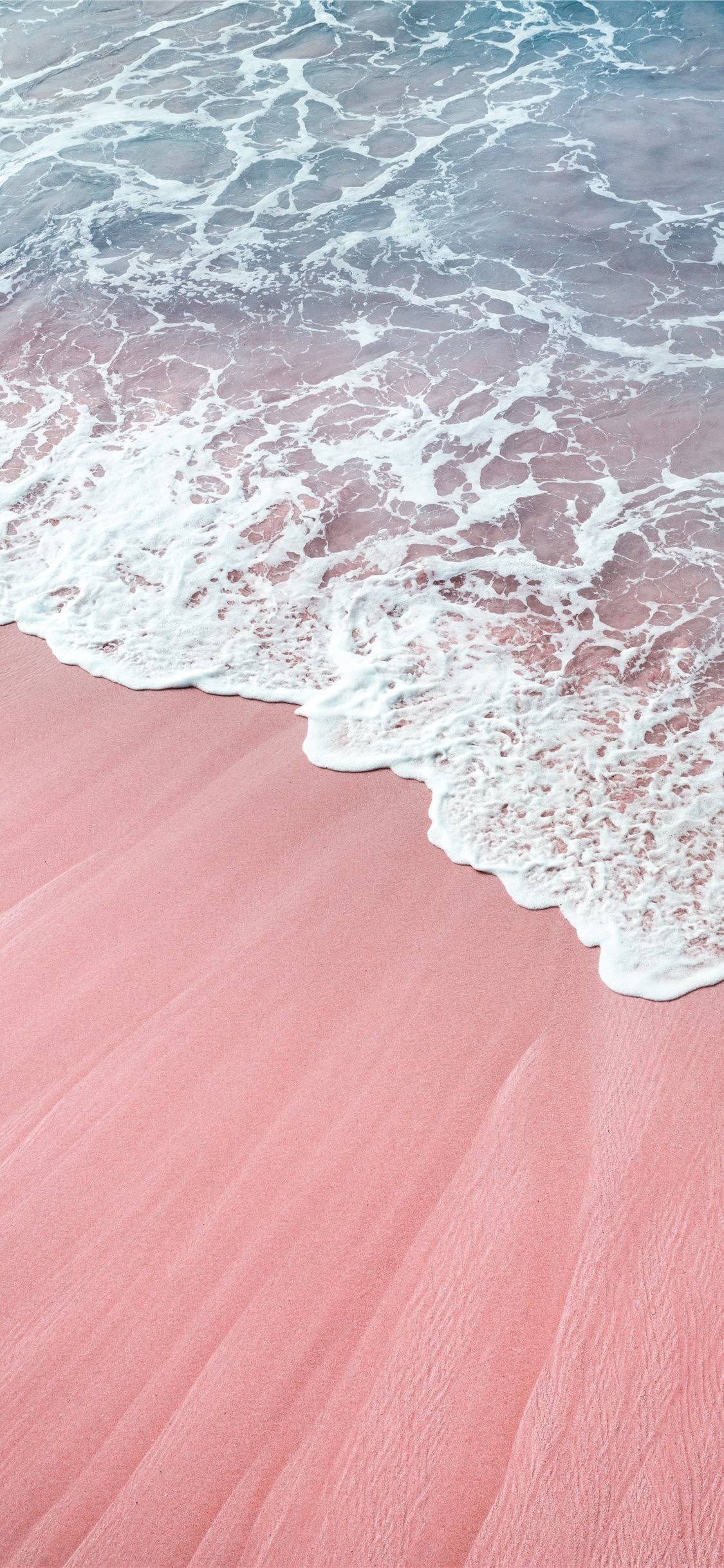 Pink iPhone Xr 桌布 壁紙 — 粉紅沙灘，泡沫般的白色海浪在柔和日光下輕輕翻滾。
