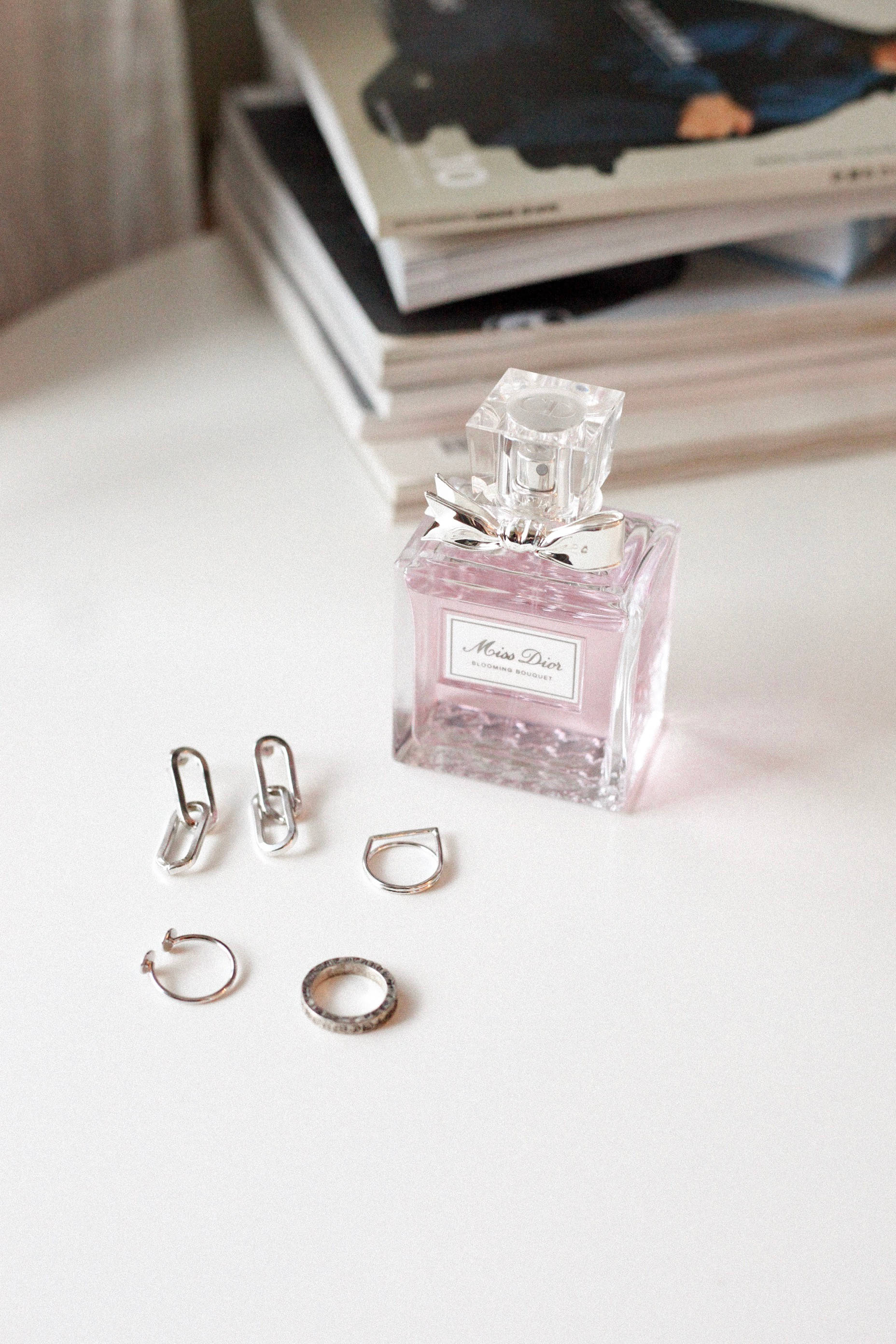 Dior 動態 桌布 壁紙 — 粉紅色 Miss Dior 香水瓶和銀色首飾放在白色表面上，旁邊有疊起的雜誌。