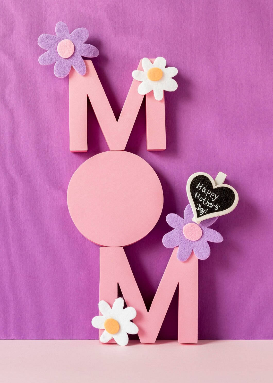m 桌布 壁紙 — 粉紅色 'MOM' 字母，飾以絨花和一個寫著 'Happy Mother's Day' 的黑板心形，背景為鮮豔的紫色。