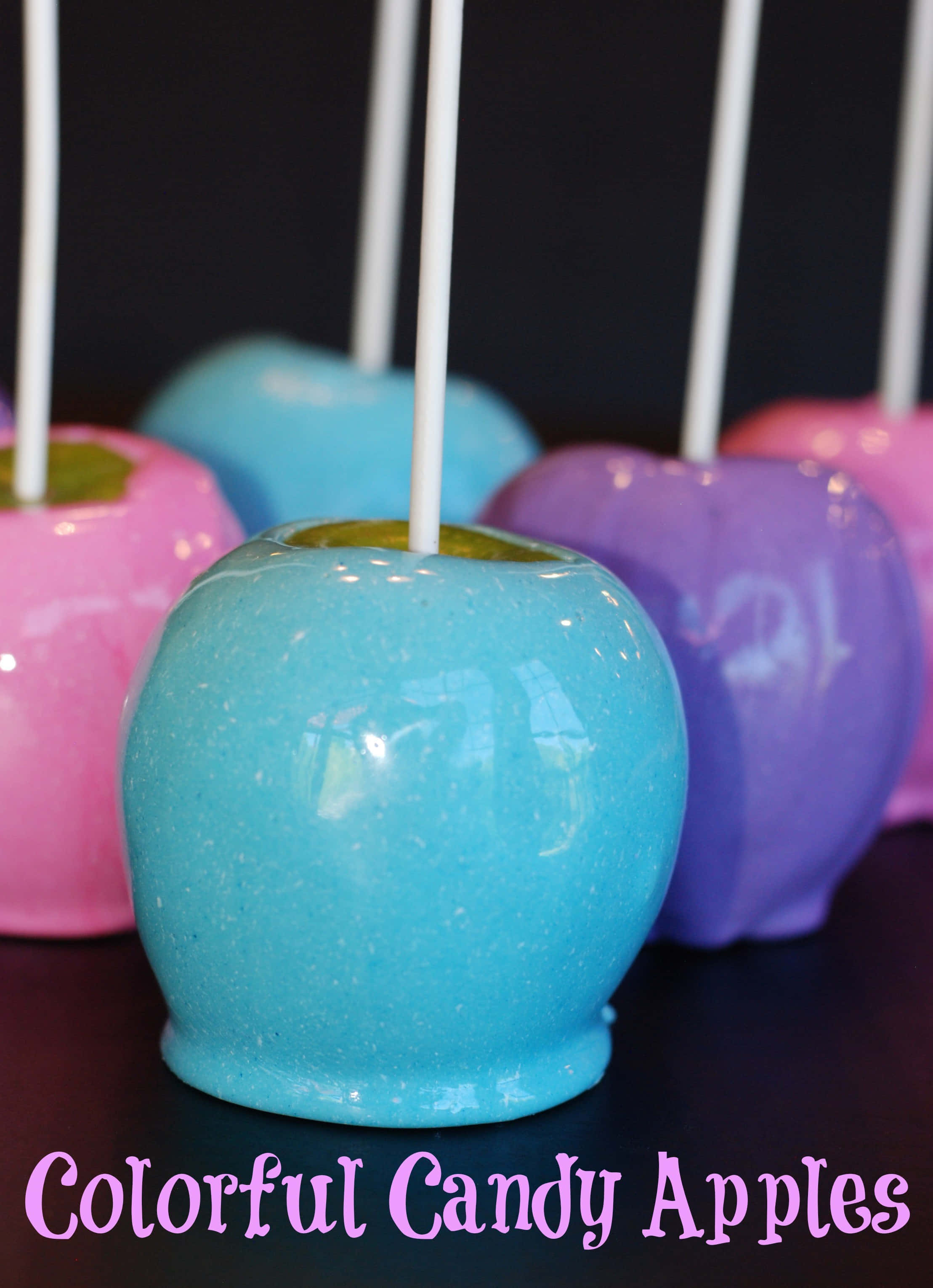 Candy Apples 桌布 壁紙 — 粉紅色、藍色和紫色的鮮豔糖果蘋果，帶有白色棒，排列在深色表面上。