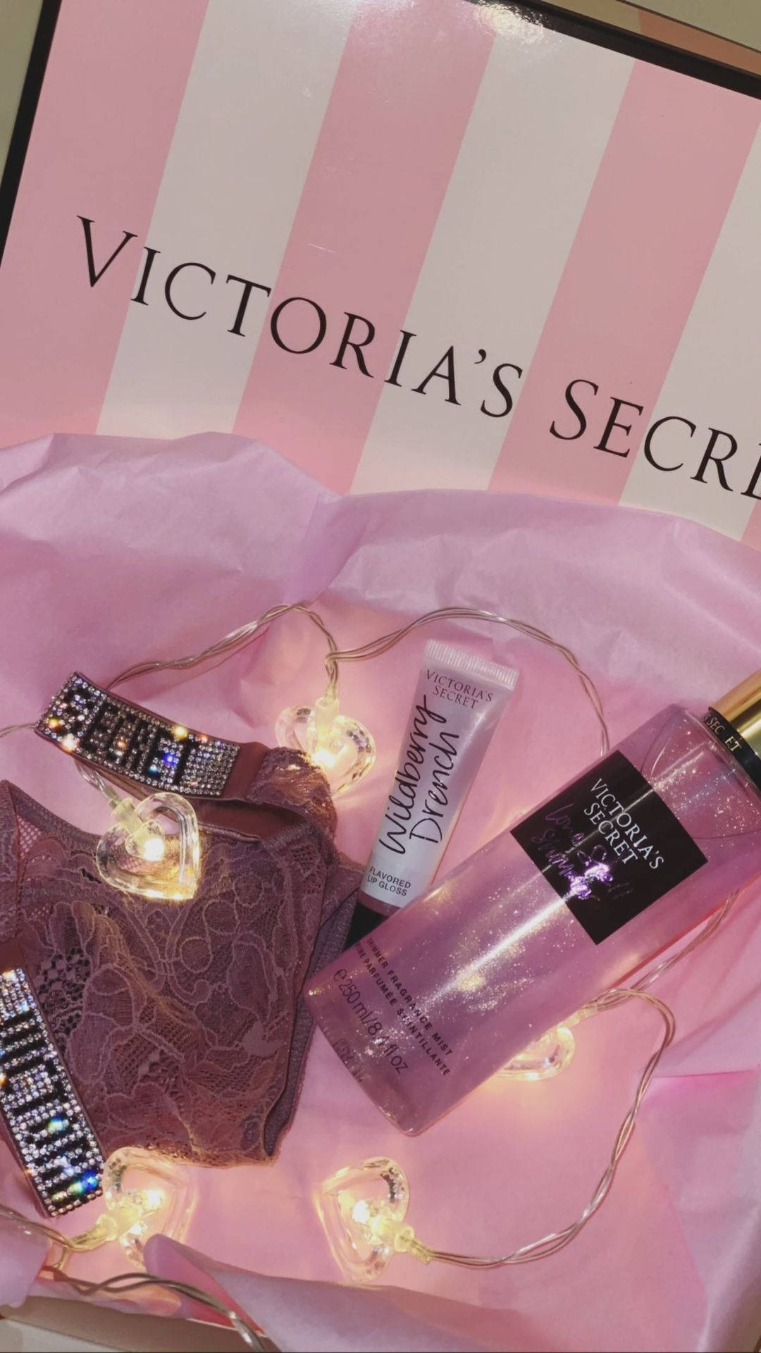 victoria 桌布 壁紙 — 粉紅色Victoria's Secret內衣及身體產品在粉紅色紙巾上的串燈下發光。