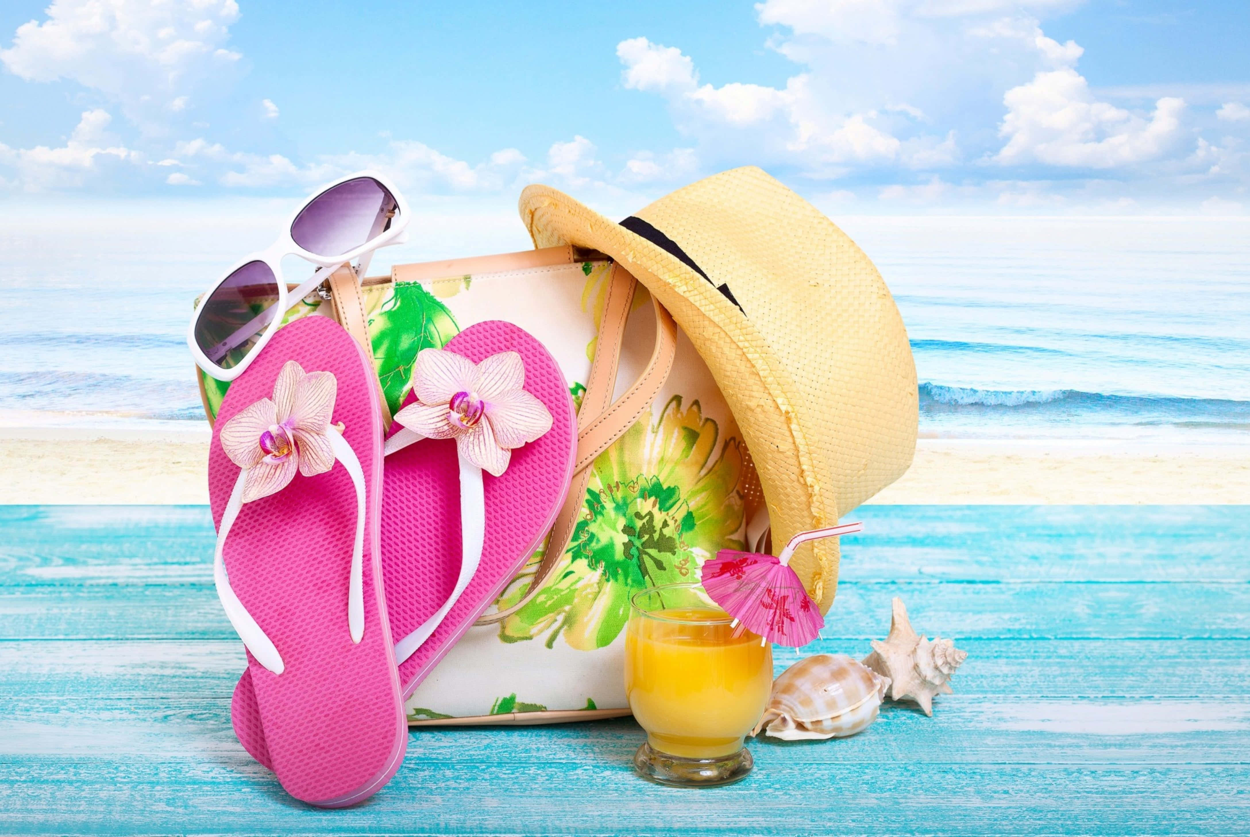 Beach Accessories 桌布 壁紙 — 粉紅色人字拖、太陽眼鏡、草帽和熱帶飲料放在經風化的藍色木頭上，背景是陽光明媚的海灘。