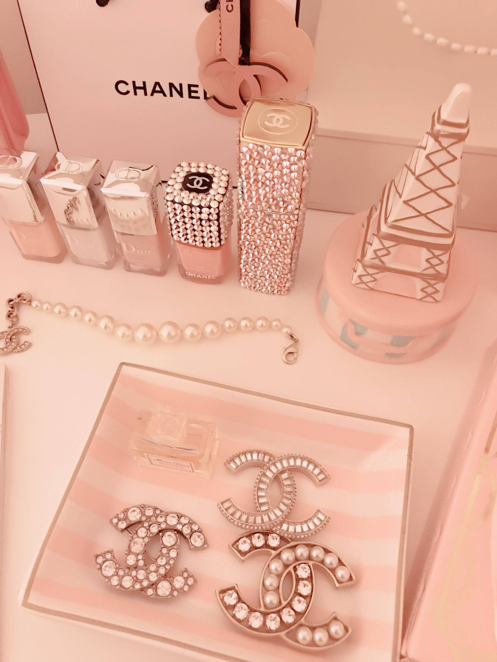 玫瑰金 桌布 壁紙 — 粉紅色化妝台展示，配有Chanel和Dior化妝品、珍珠首飾和標誌性Logo配件，排列在條紋托盤上。
