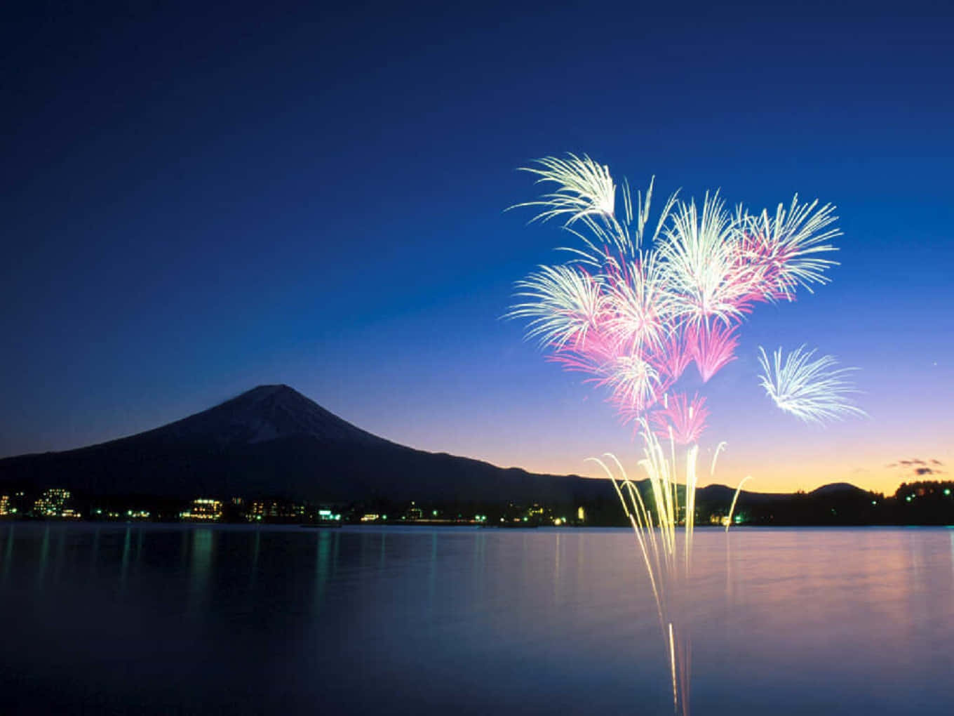 Fireworks 桌布 壁紙 — 粉紅色和白色的煙火在平靜的湖面上綻放，富士山的剪影映襯在暮色天空中。