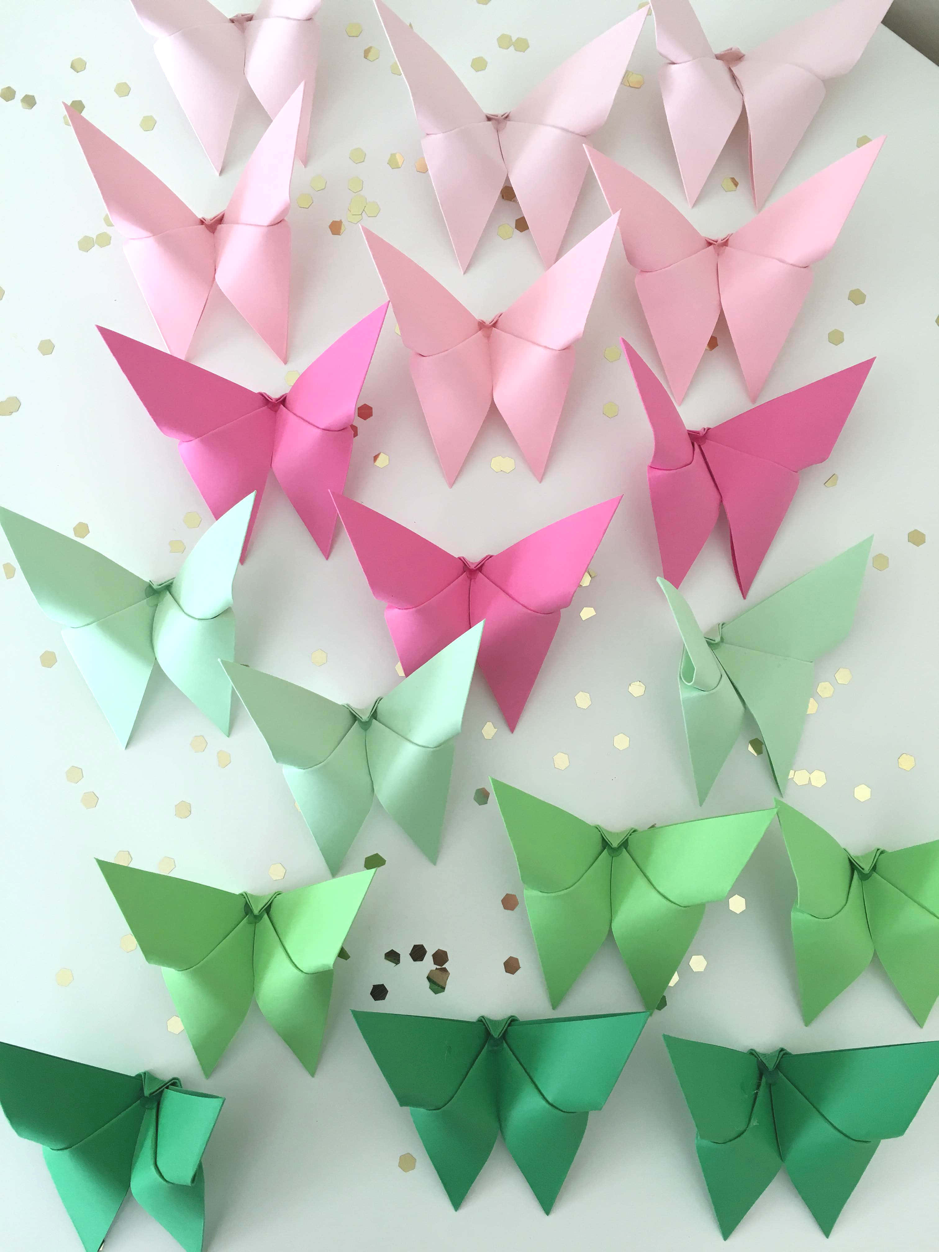 Butterfly Origami 桌布 壁紙 — 粉紅色和綠色的摺紙蝴蝶在白色表面上排列成行，並散落著金色紙屑的鮮豔漸變。