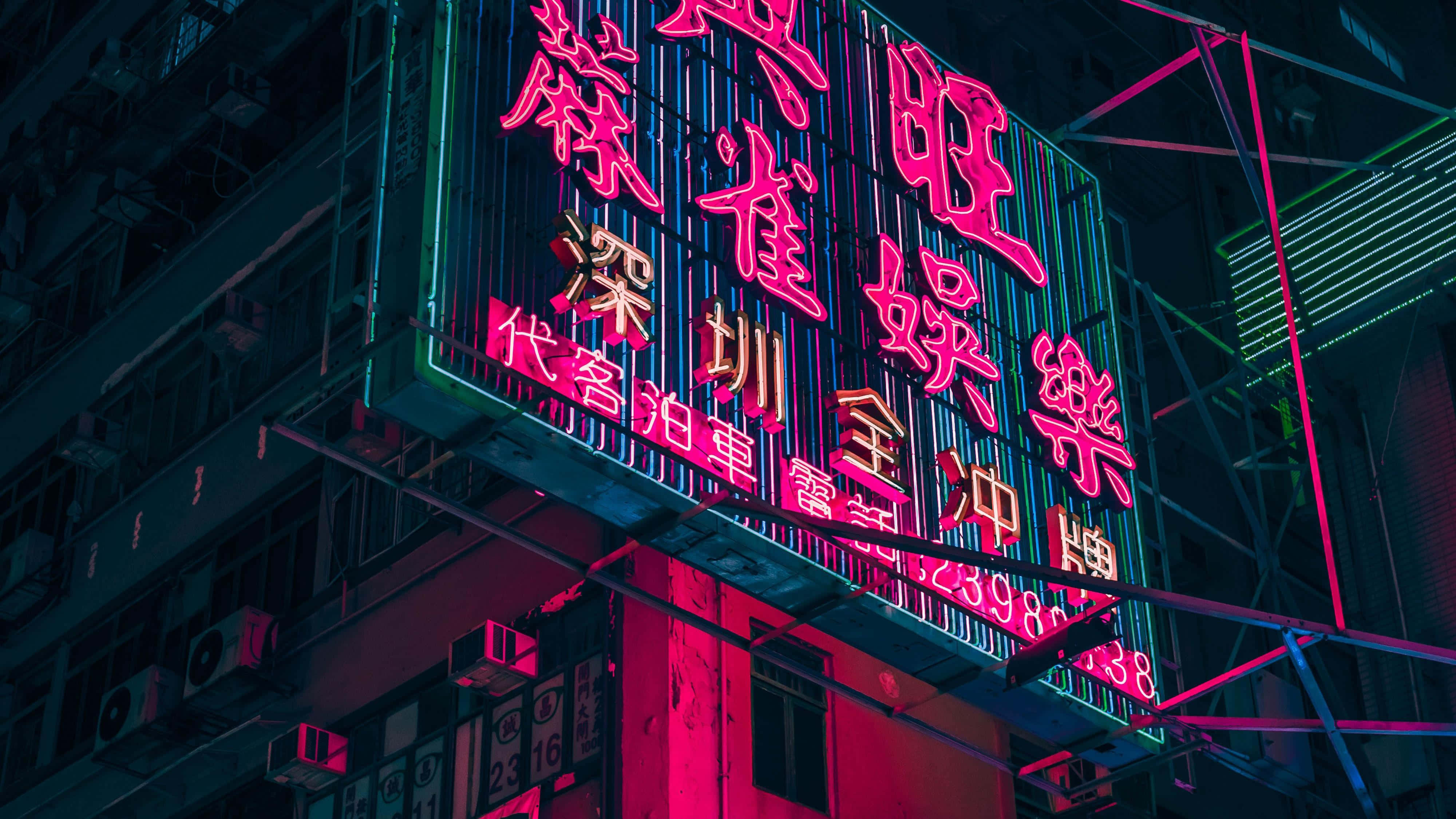Aesthetic Computer 4K 桌布 壁紙 — 粉紅色和綠色的鮮豔霓虹燈在夜間照亮黑暗的城市建築外牆。