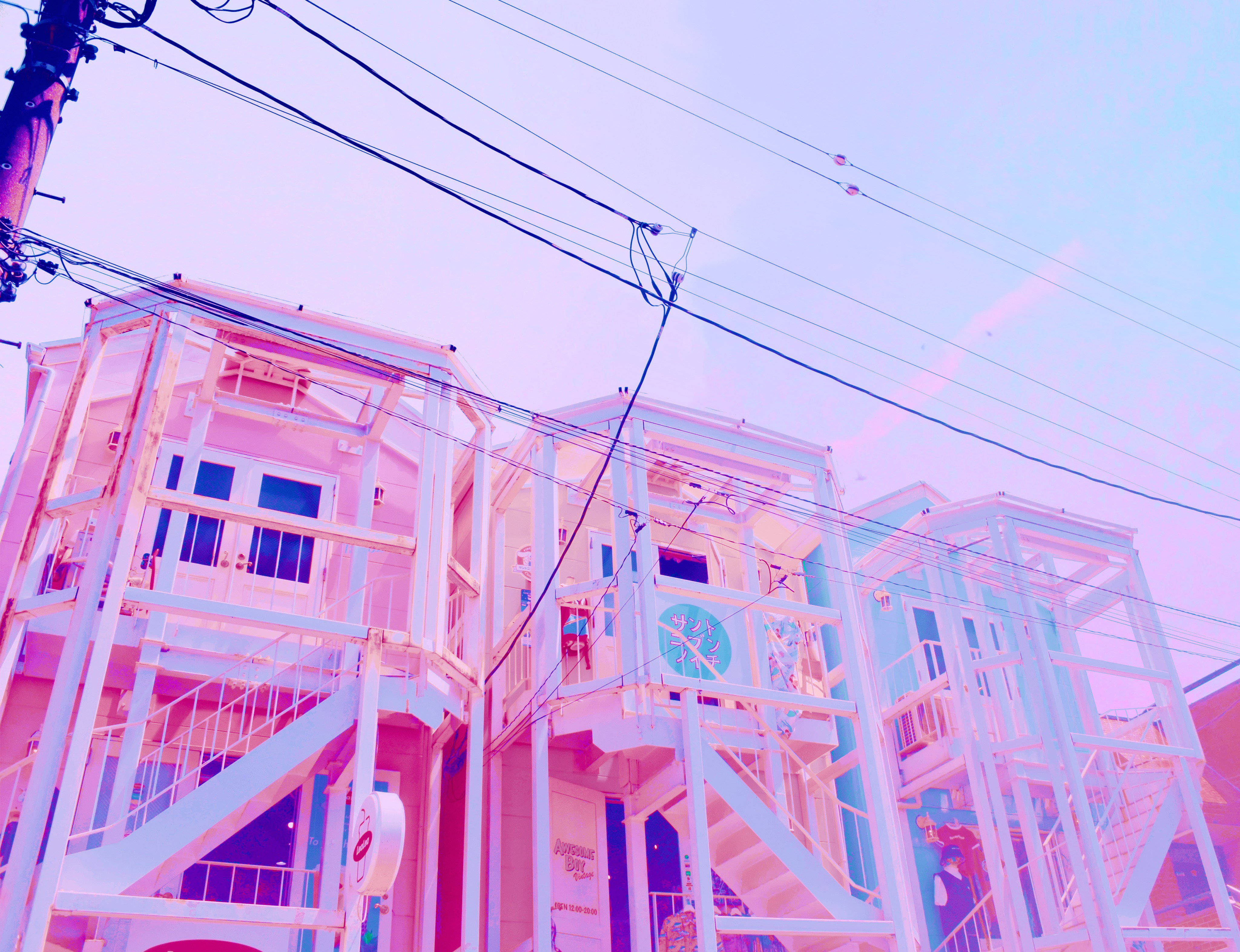 Buildings 桌布 壁紙 — 粉紅色和藍色建築物，設有外部樓梯，天空朦朧，有架空電線。