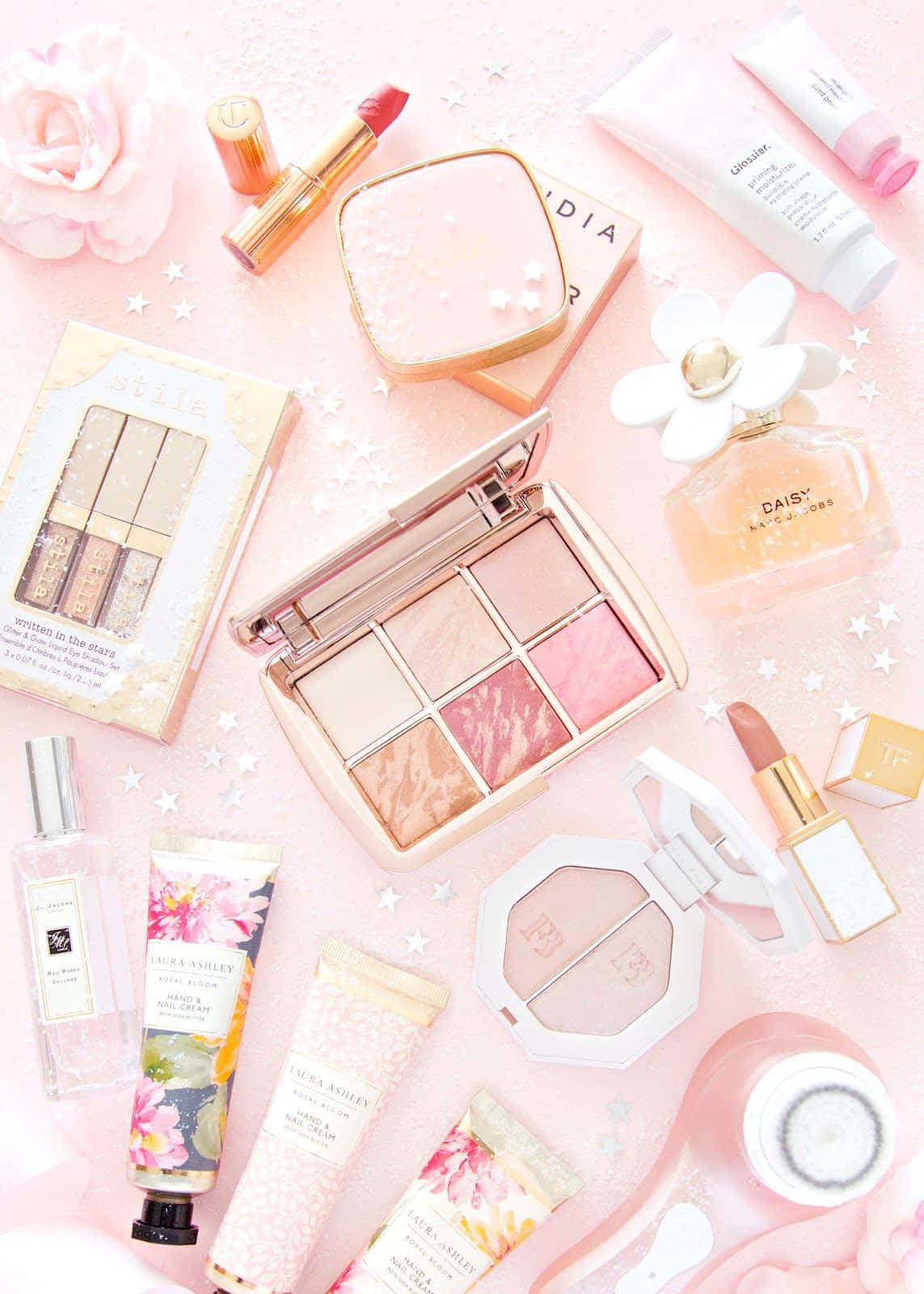 Cute Makeup 桌布 壁紙 — 粉紅色和金色的美容產品散落在粉彩粉紅色表面上，帶有白色星星和玫瑰的平鋪佈局。