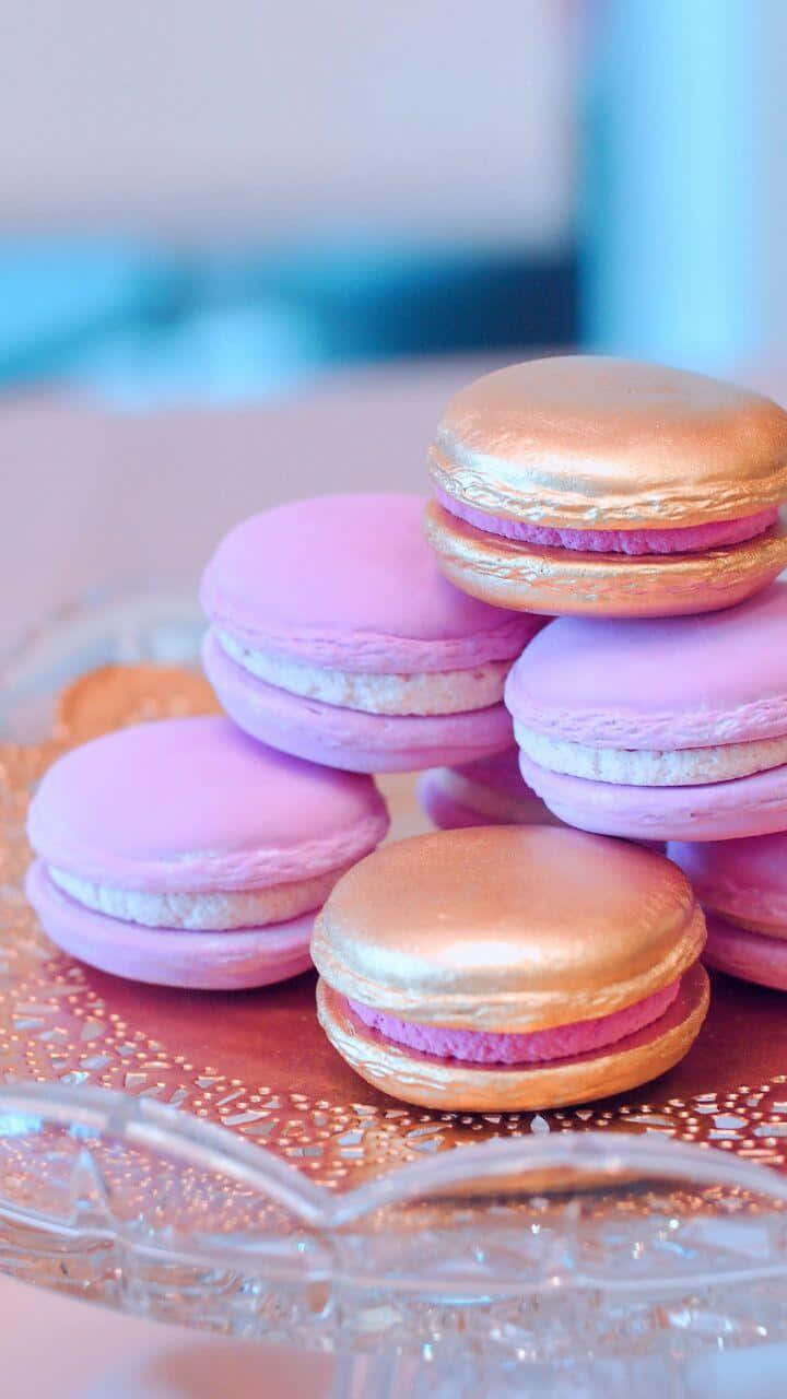 Macaron 桌布 壁紙 — 粉紅色和金色的馬卡龍堆疊在一起，內餡是白色奶油，放在玻璃蛋糕架上。