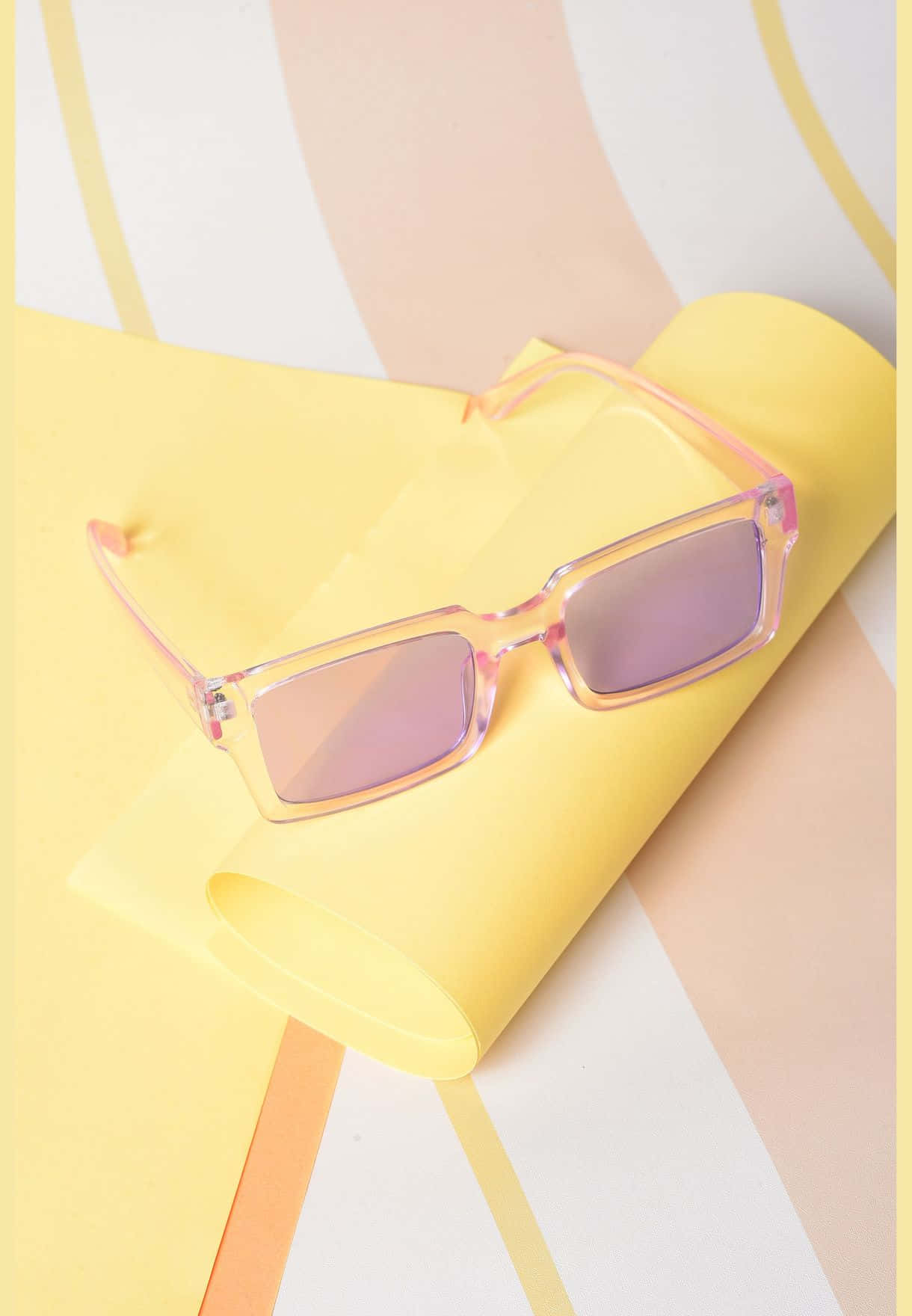 Purple Sunglasses 桌布 壁紙 — 粉紅色太陽眼鏡放在一張捲起的黃色紙上，背景是柔和幾何圖案的蜜桃白和黃色條紋。