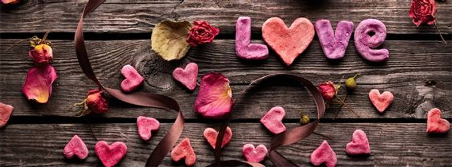 Facebook Cover 桌布 壁紙 — 粉紅色心形糖果在質樸的木質表面上拼出love，周圍環繞著乾燥玫瑰花瓣和絲帶。