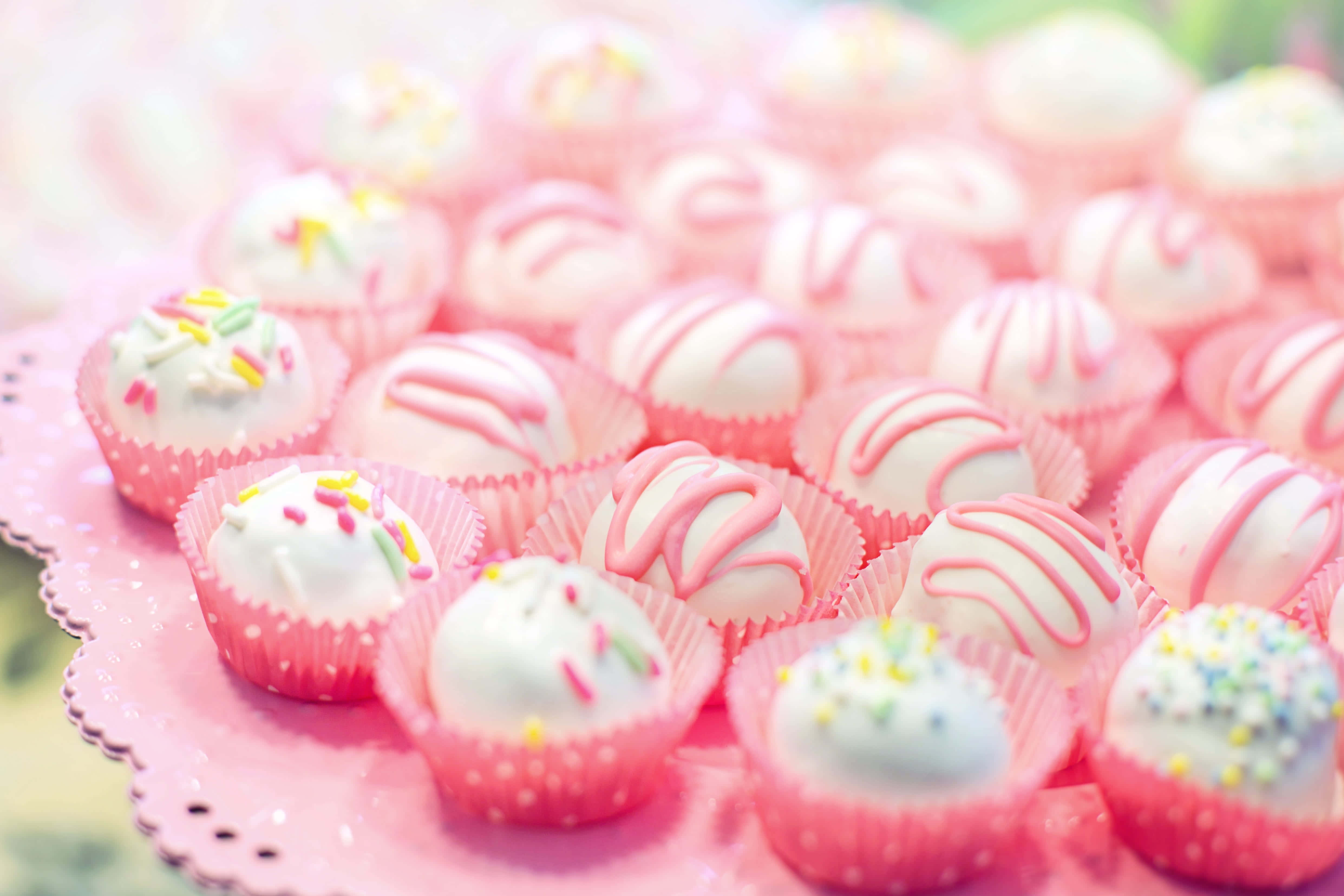 Pink Cupcakes 桌布 壁紙 — 粉紅色扇貝邊盤子上，粉紅色紙杯蛋糕襯墊裝著帶有粉紅色漩渦和彩色糖粒的白巧克力松露的特寫。