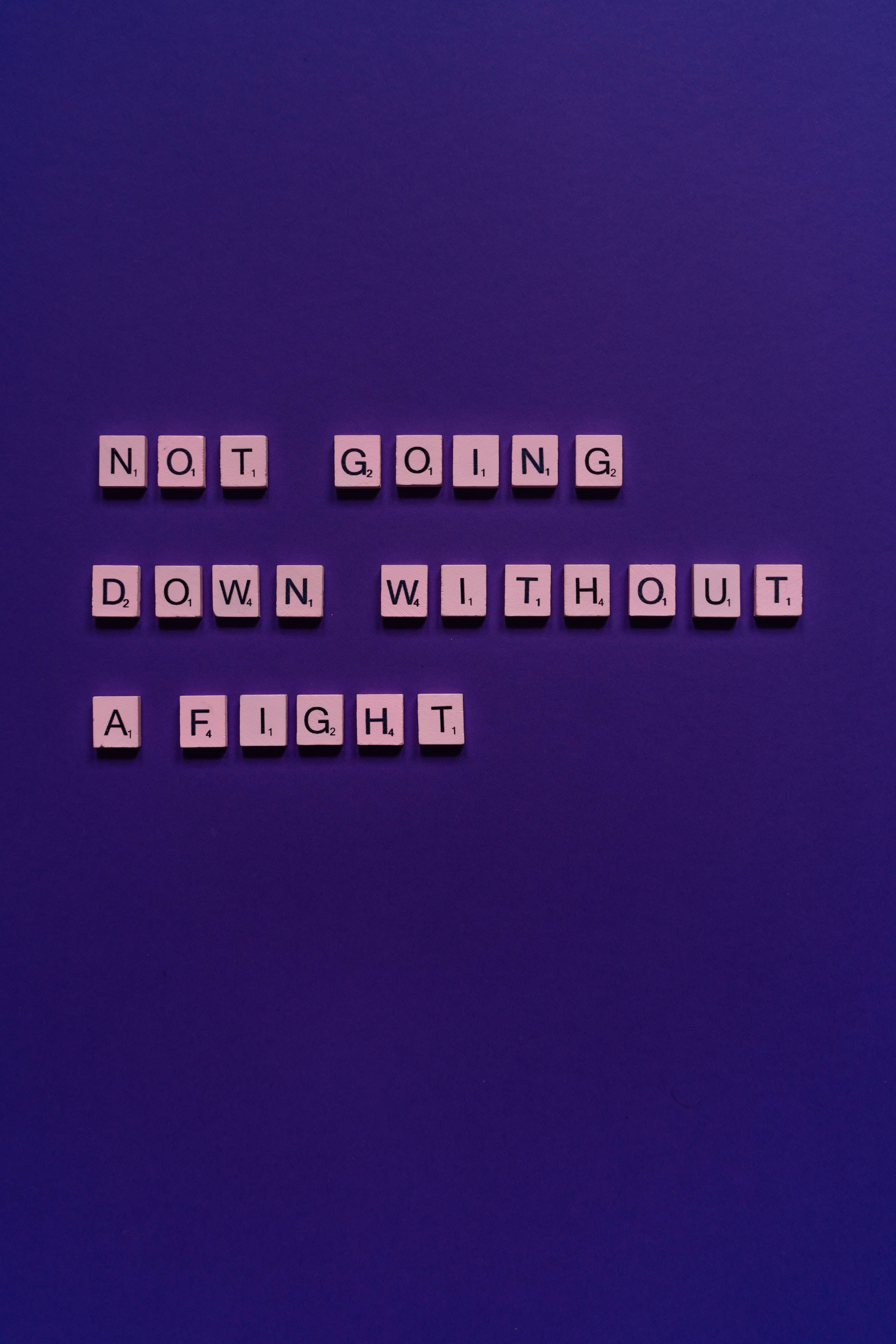 Quote 桌布 壁紙 — 粉紅色拼字磚在深紫色背景上拼出「NOT GOING DOWN WITHOUT A FIGHT」。
