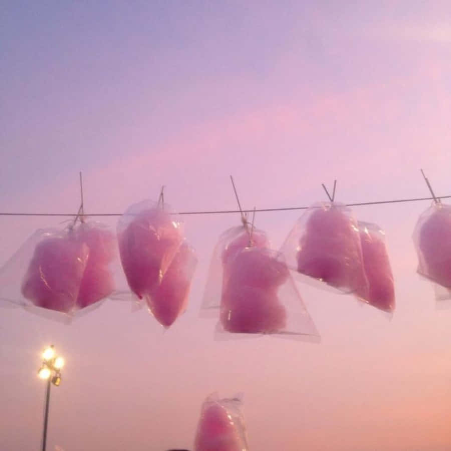 Pastel Pink Aesthetic 桌布 壁紙 — 粉紅色棉花糖袋掛在鐵線上，背景是柔和的紫色和粉紅色暮色天空，下方有路燈閃耀。