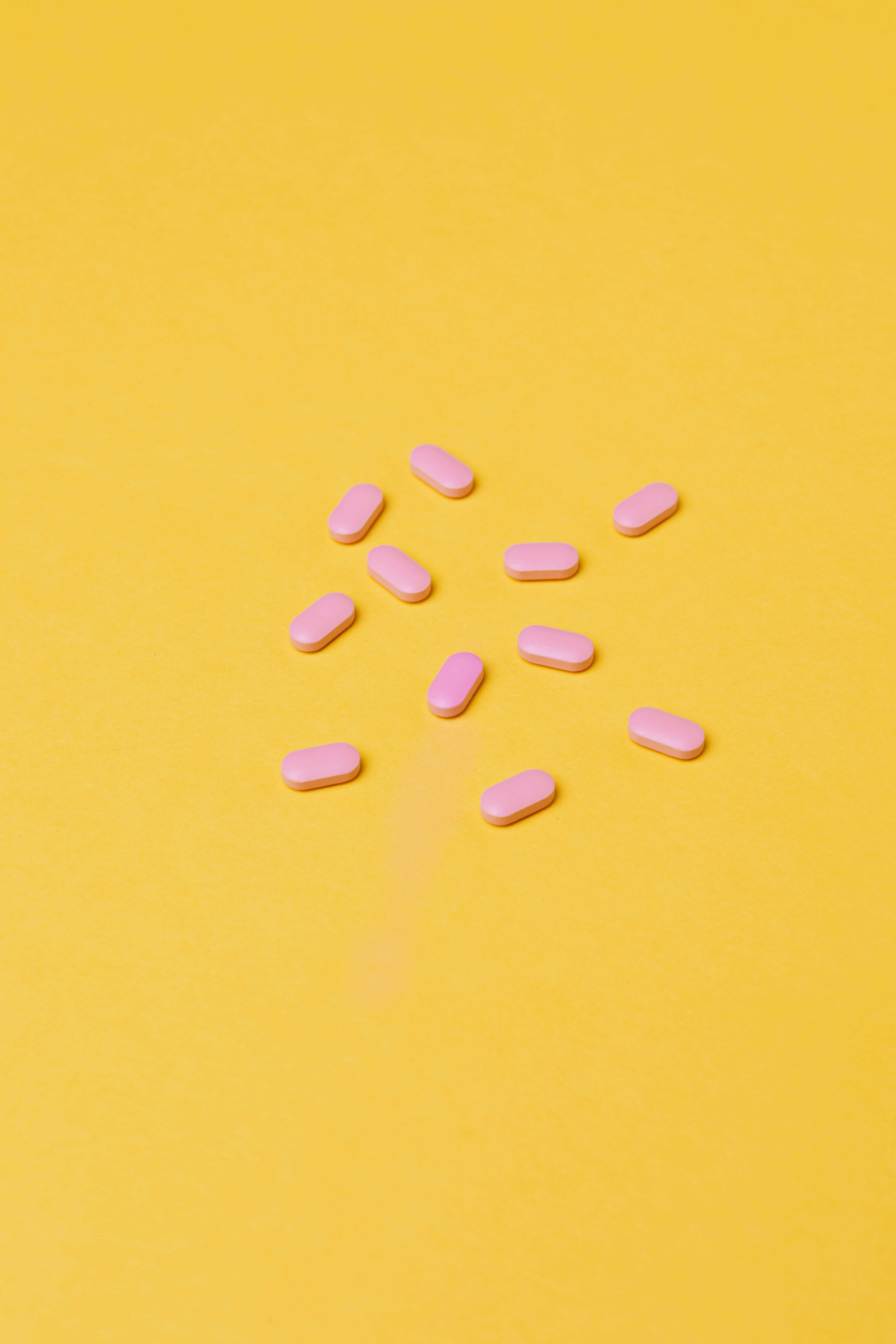 Pastel Pink And Yellow 桌布 壁紙 — 粉紅色橢圓形藥丸隨意散落在充滿活力的黃色背景上，形成極簡的平鋪構圖。