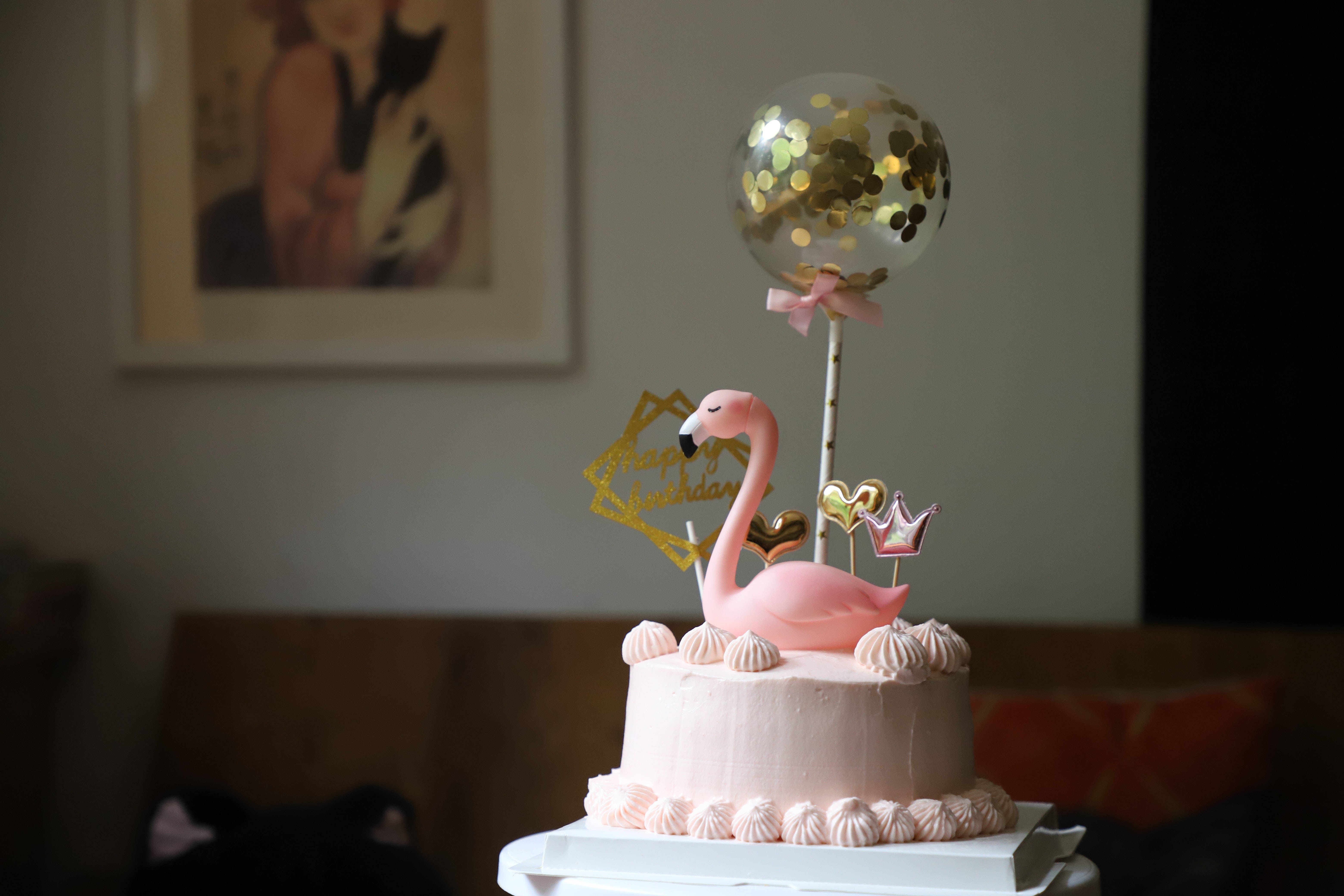Birthday Cake 桌布 壁紙 — 粉紅色火鶴裝飾點綴著一個精緻的粉紅色糖霜生日蛋糕，上面裝飾著金色紙屑和皇冠裝飾。